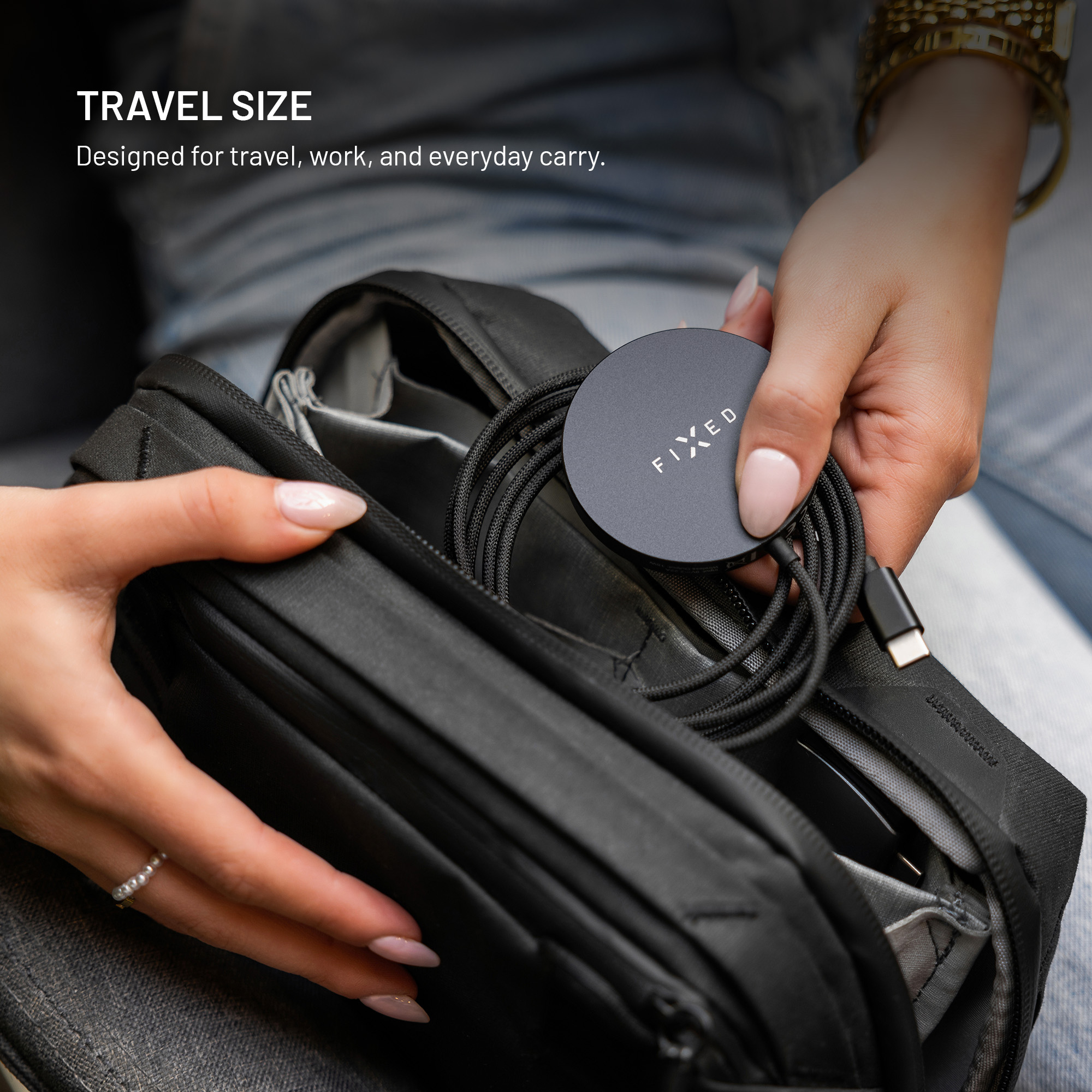 Eine Person packt ein rundes, schwarzes Fixed-Ladegerät mit aufgewickeltem Kabel in eine Reisetasche.