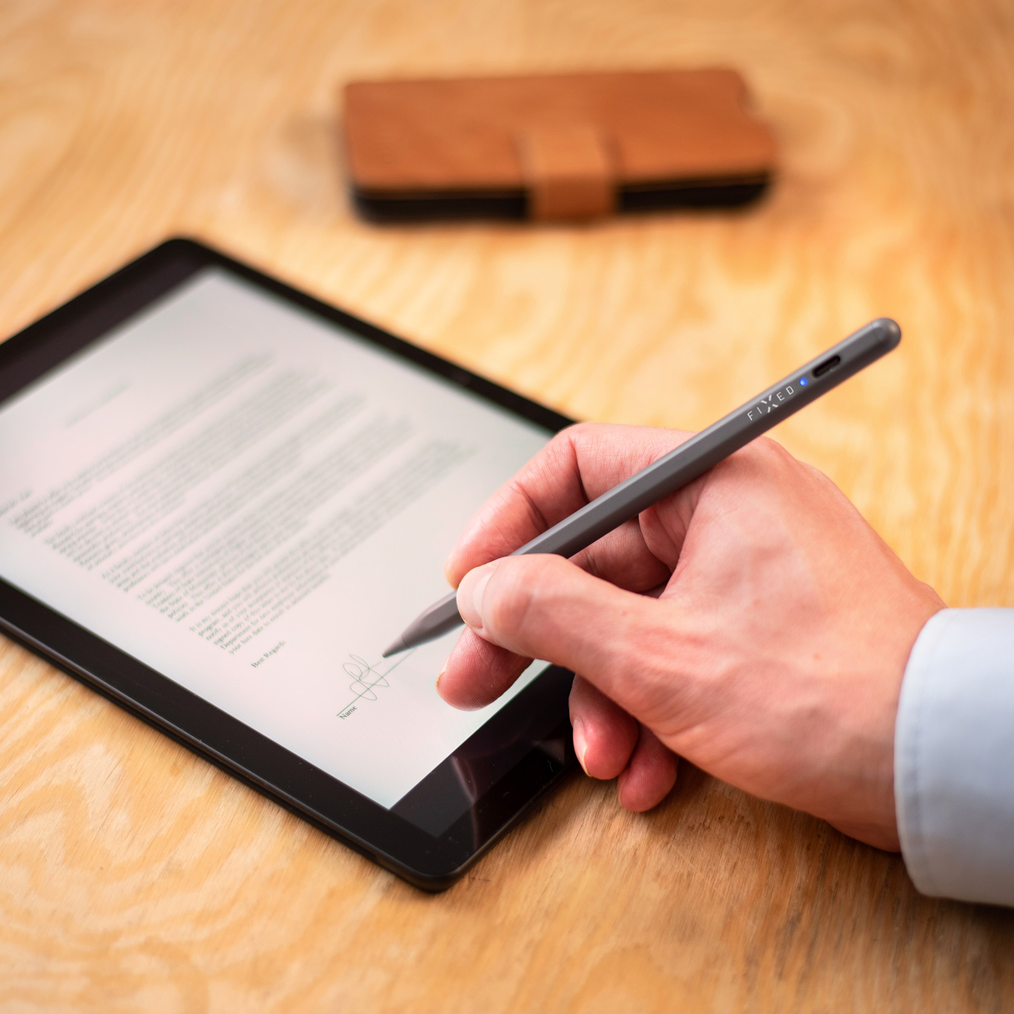 Hand unterschreibt ein Dokument auf einem Tablet mit einem Eingabestift auf Holztisch.
