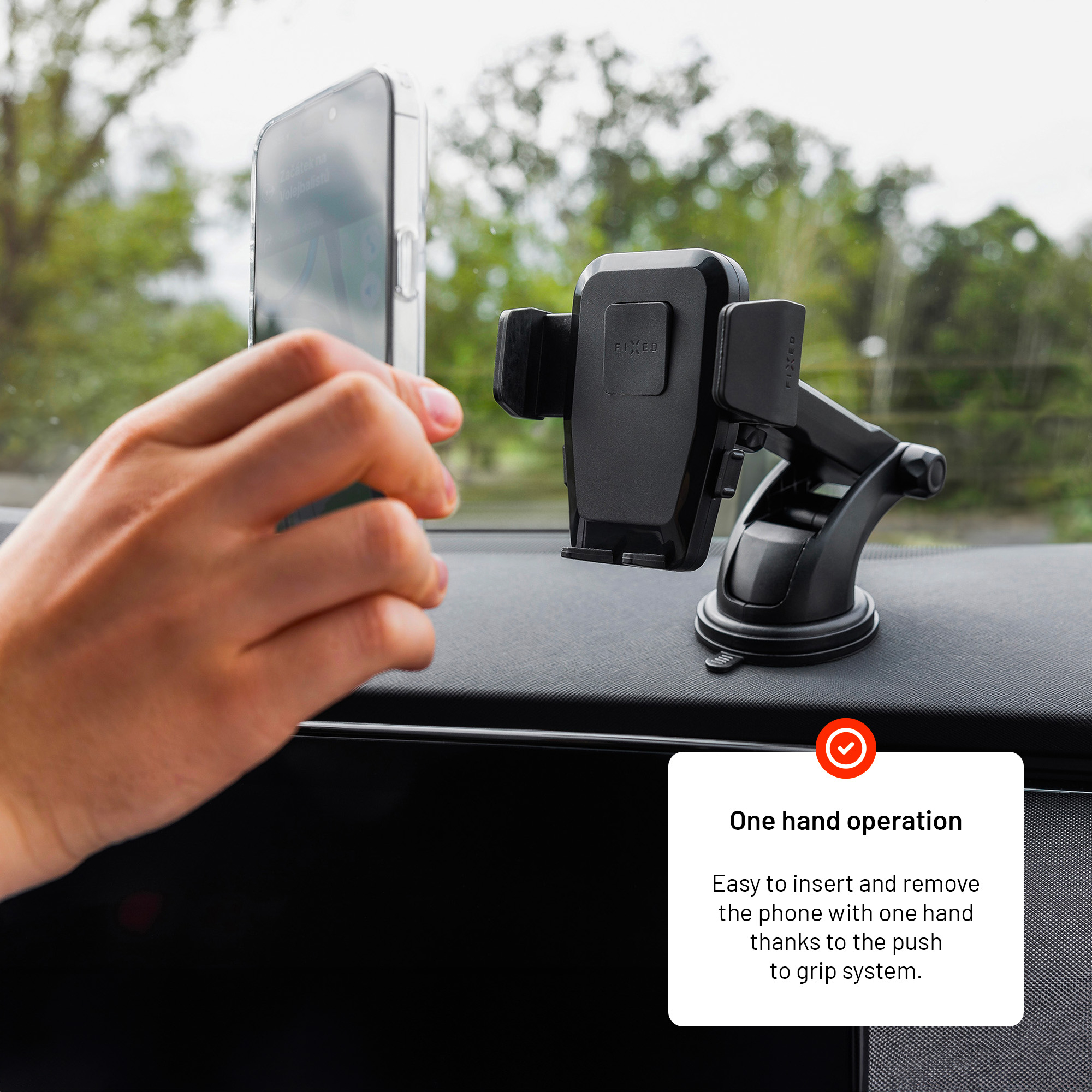 Hand hält ein Smartphone in der Nähe einer schwarzen Kfz-Handyhalterung auf einem Armaturenbrett.