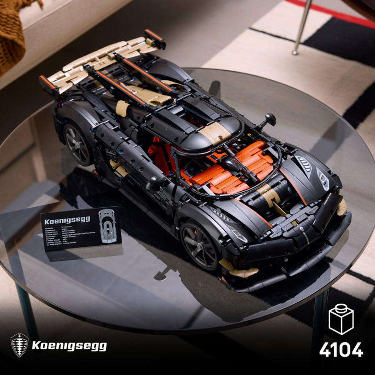 Un coche modelo Lego Technic Koenigsegg negro y dorado sobre una mesa de vidrio junto a una placa informativa.