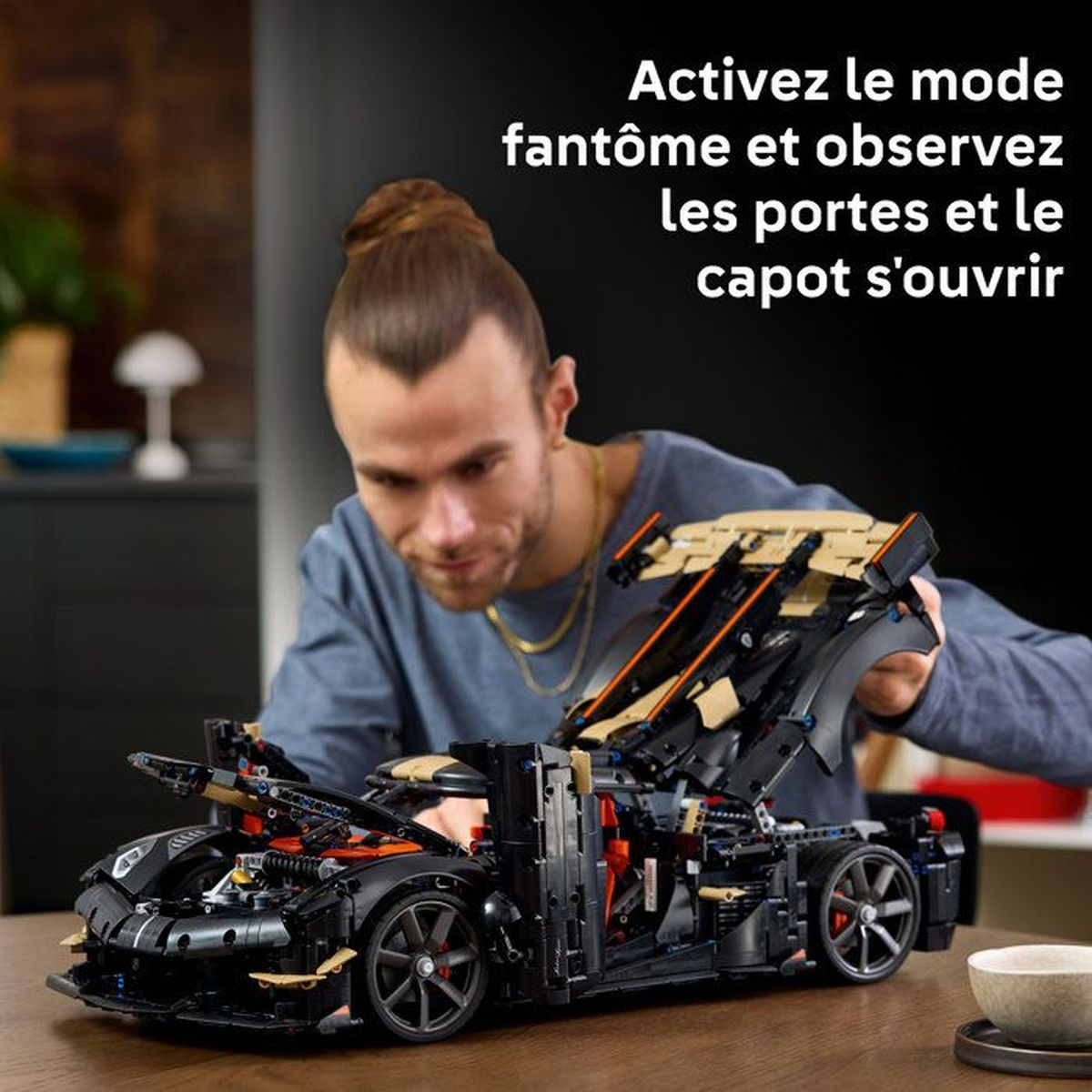 Un hombre construyendo un coche Lego Technic negro en una mesa de madera.
