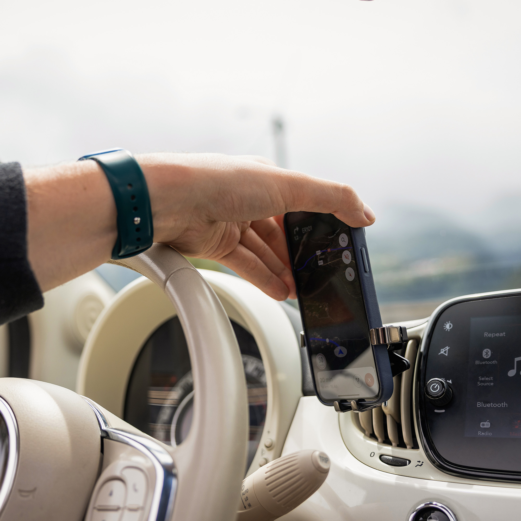 Fahrer platziert ein Smartphone in der Halterung am Armaturenbrett eines Autos mit hellem Interieur.