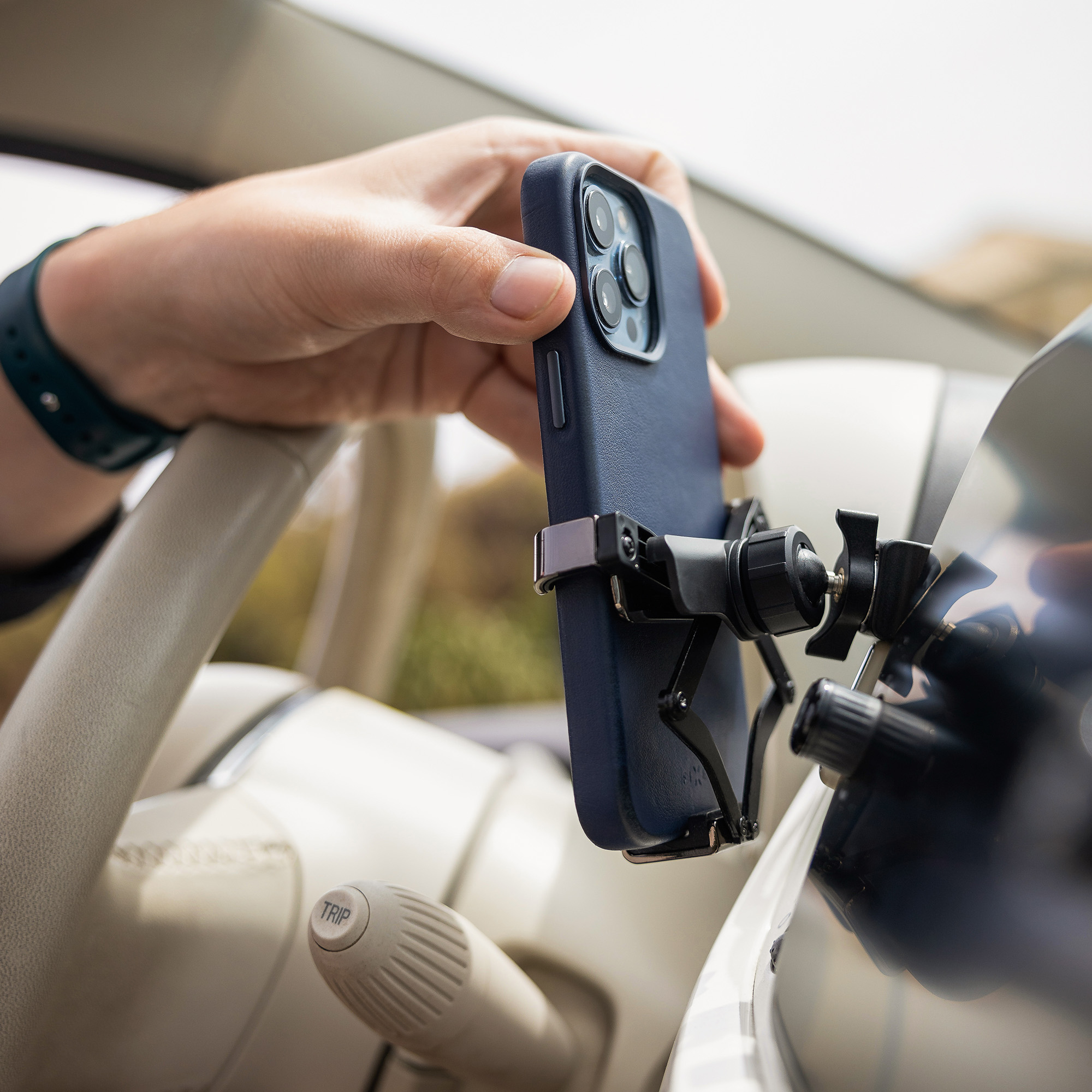 Eine Hand setzt ein blaues Smartphone in eine Halterung am Armaturenbrett eines Autos.