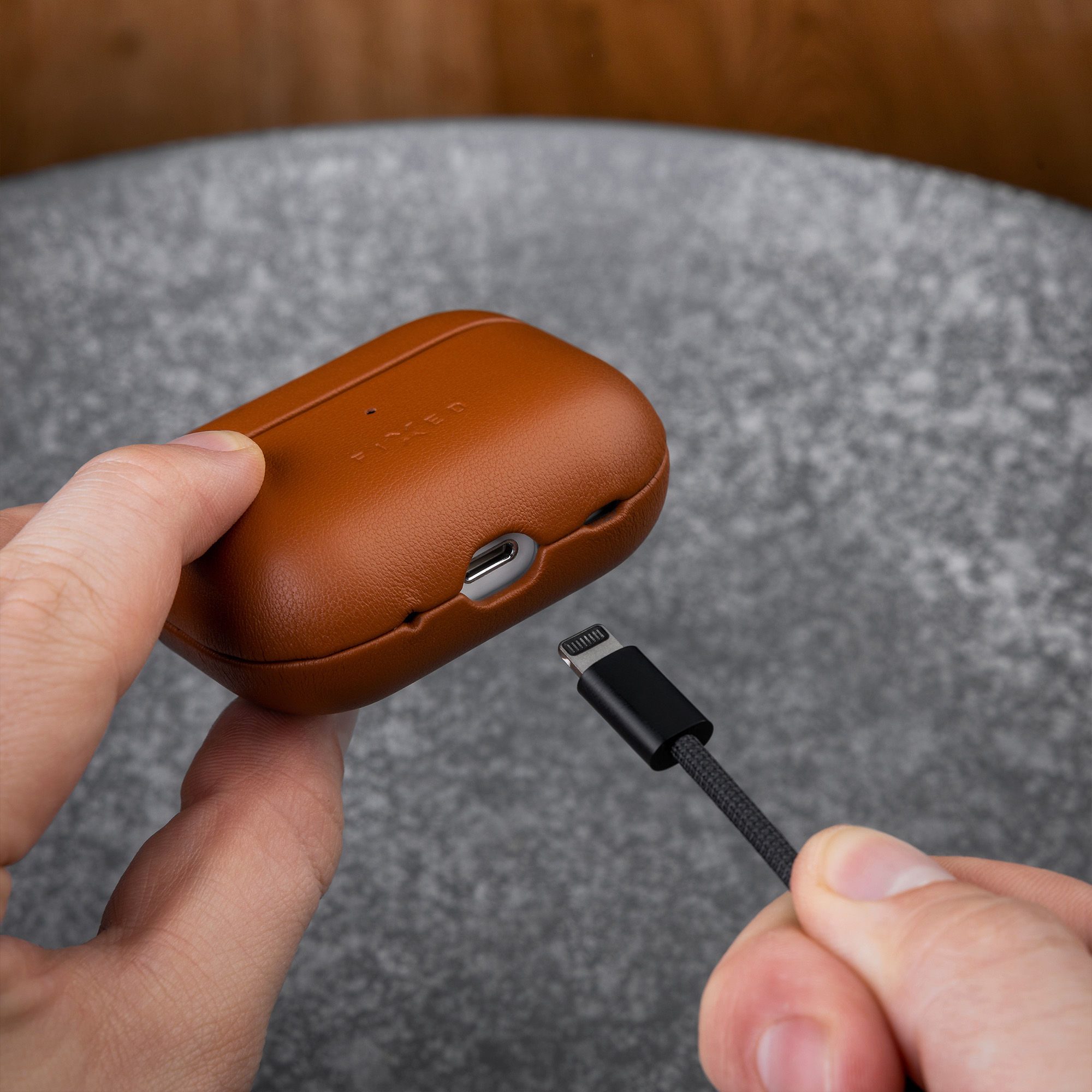 Person lädt braune Leder-AirPods-Hülle mit einem schwarzen Lightning-Kabel auf.