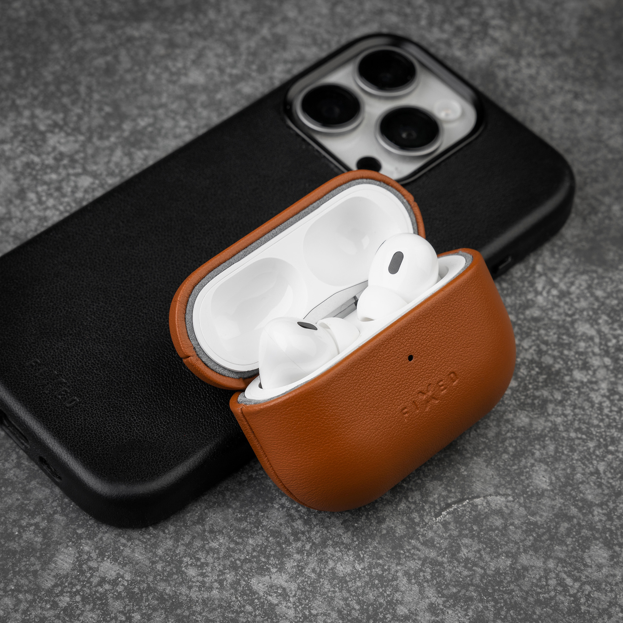 Weiße Ohrhörer im braunen Lederetui vor einem schwarzen Smartphone auf grauem Stein.