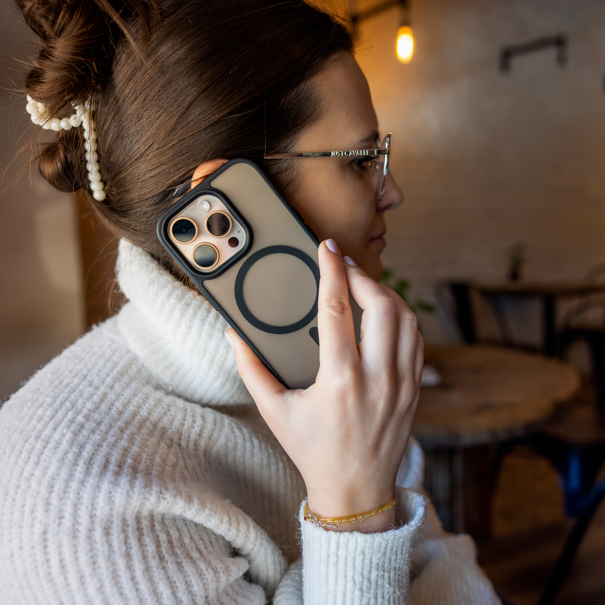 Eine Frau mit Brille und weißem Pullover telefoniert in einem Innenraum mit einem Smartphone.