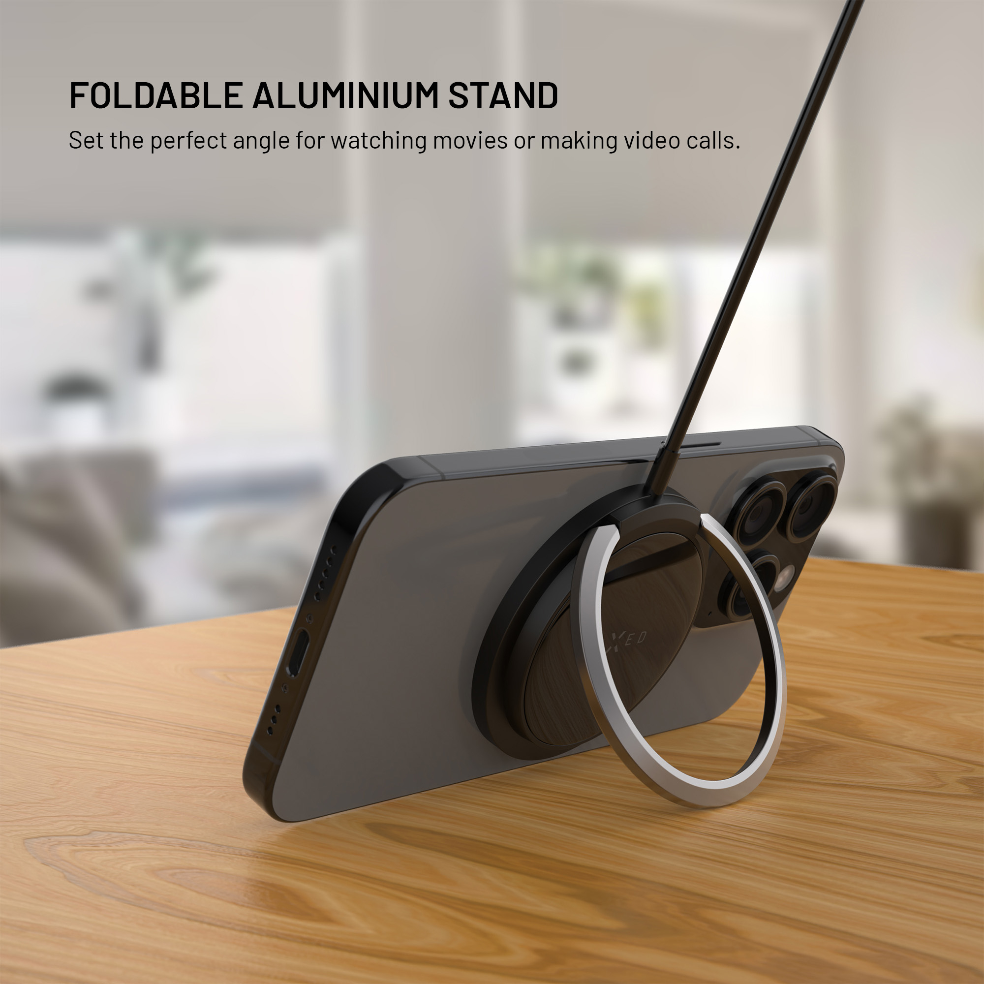 Ein Smartphone auf einem Holztisch, gestützt von einem klappbaren Aluminiumständer mit Ring.
