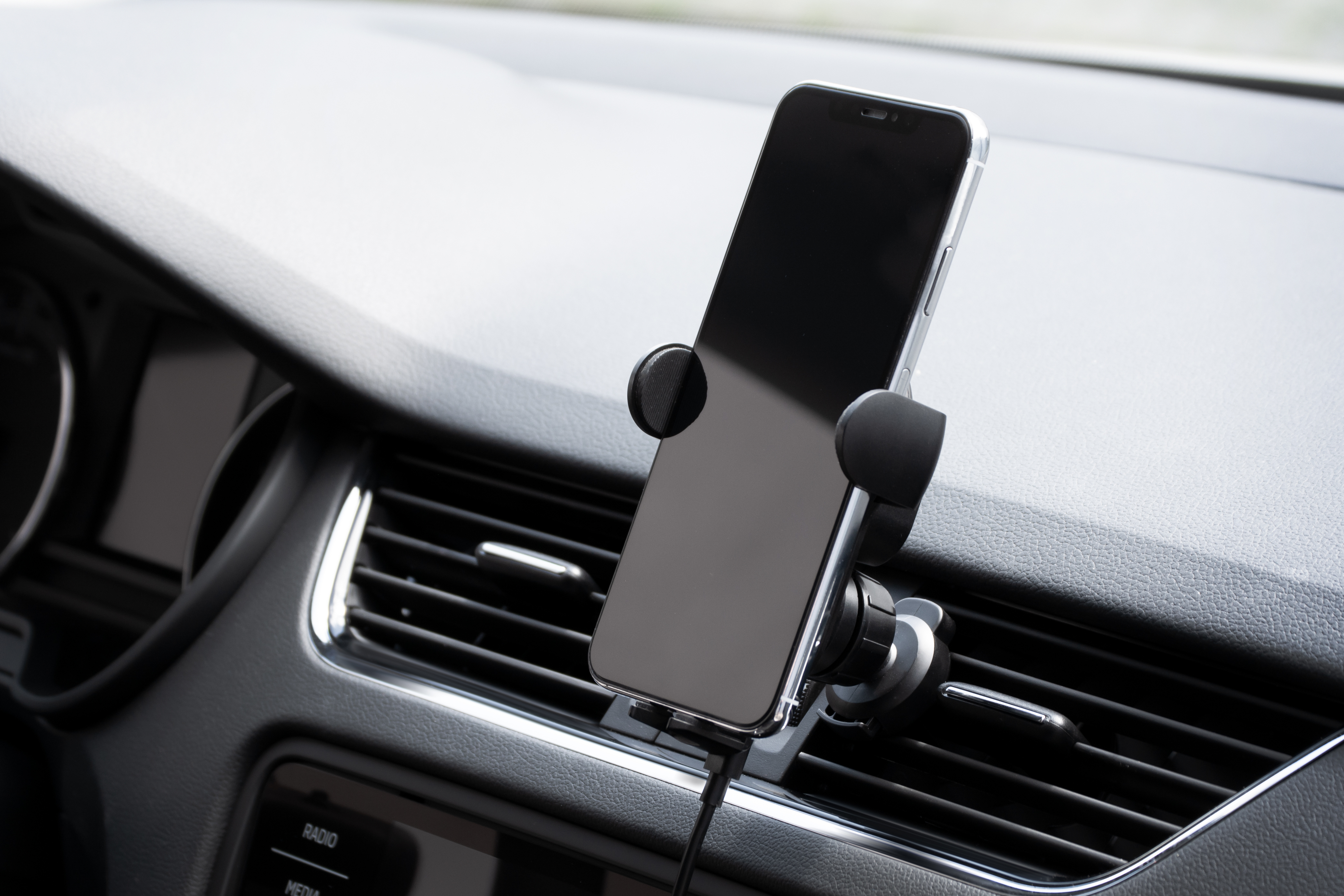 Ein Smartphone in einer Halterung, die am Lüftungsgitter des Autos befestigt ist, mit angeschlossenem Ladekabel.