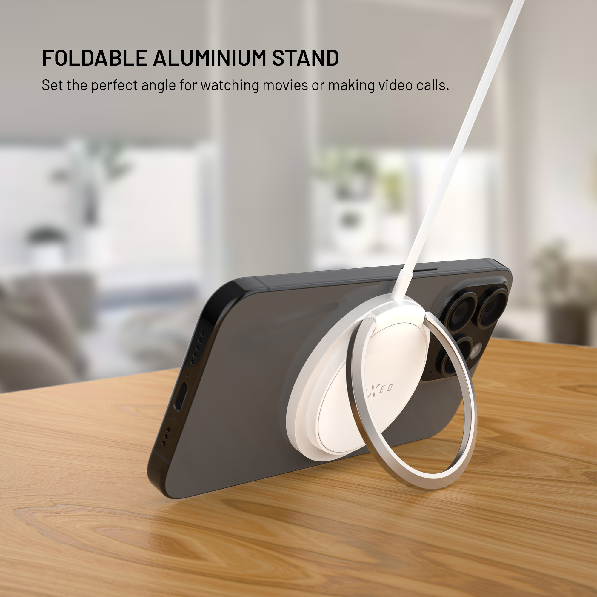 Ein Smartphone steht auf einem Holztisch, gestützt von einem runden, weißen magnetischen Ständer mit Kabel.