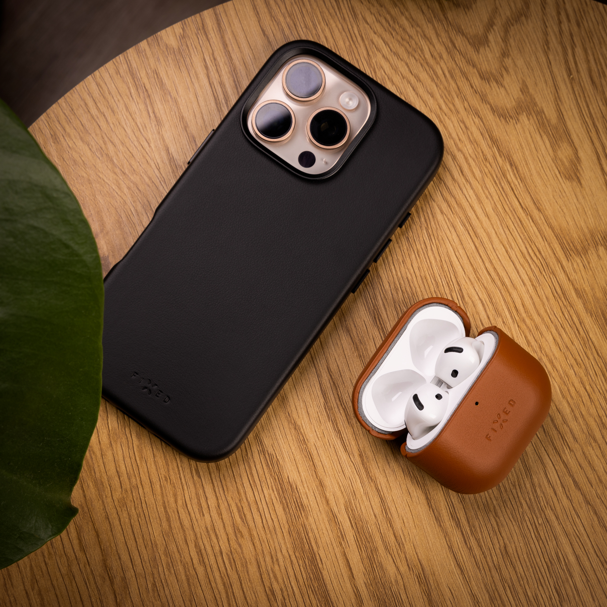 Ein schwarzes Smartphone mit Hülle und weiße Kopfhörer in einem braunen Etui liegen auf einer Holzoberfläche.