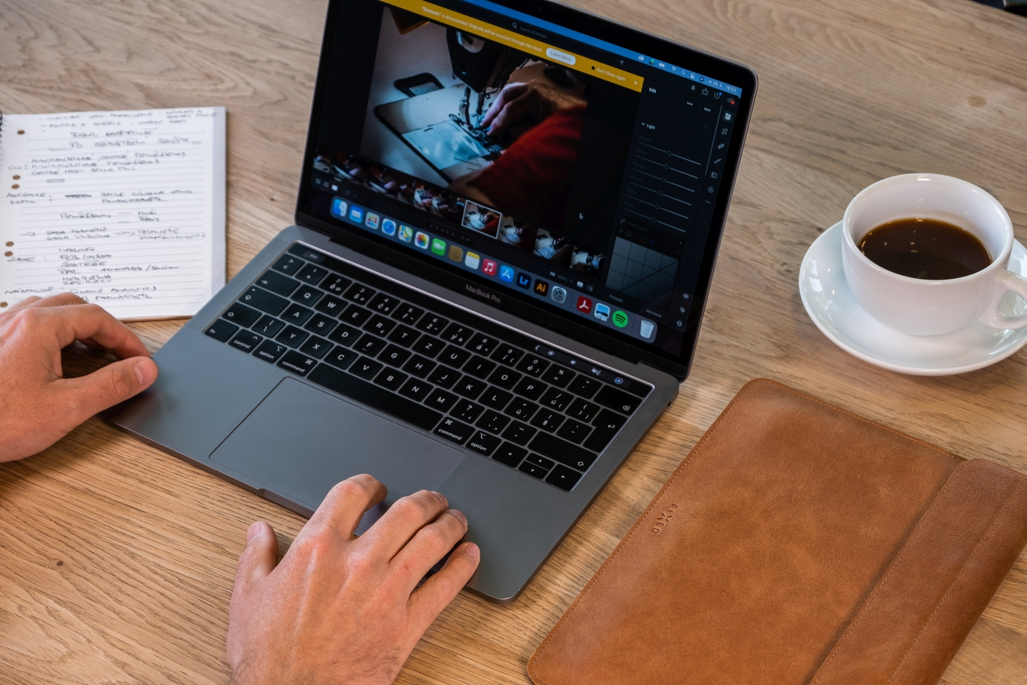 Ein Person arbeitet an einem MacBook Pro auf Holzschreibtisch mit Notizbuch und Kaffeetasse.