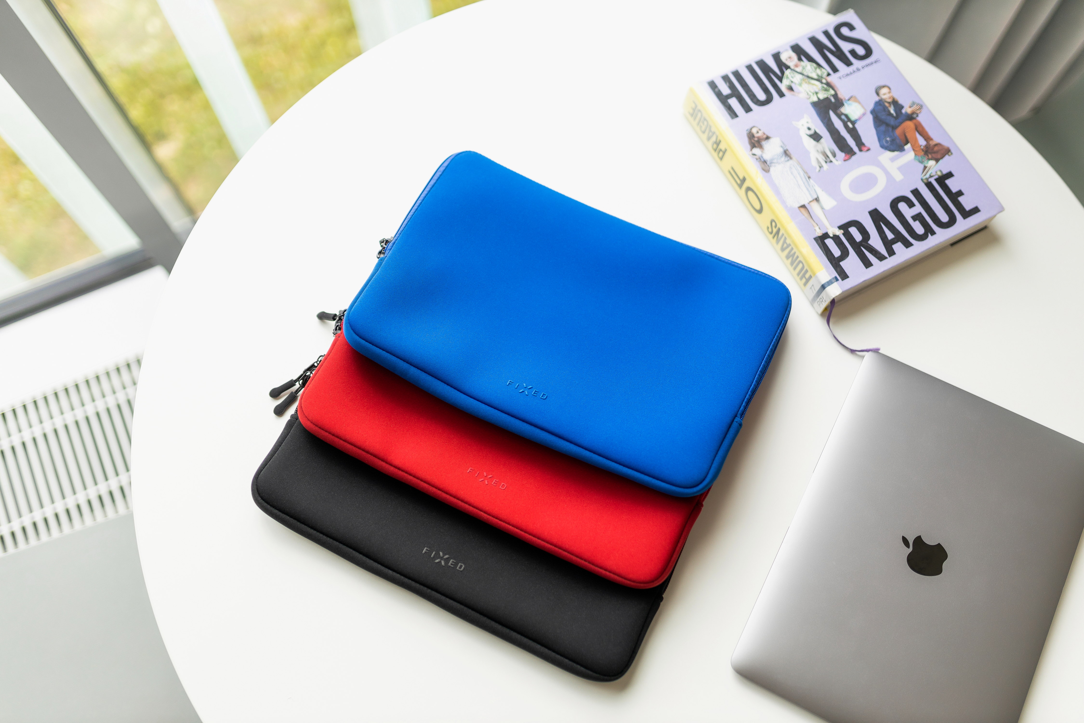 Drei gestapelte Laptopschutzhüllen in Blau, Rot und Schwarz auf einem weißen Tisch.