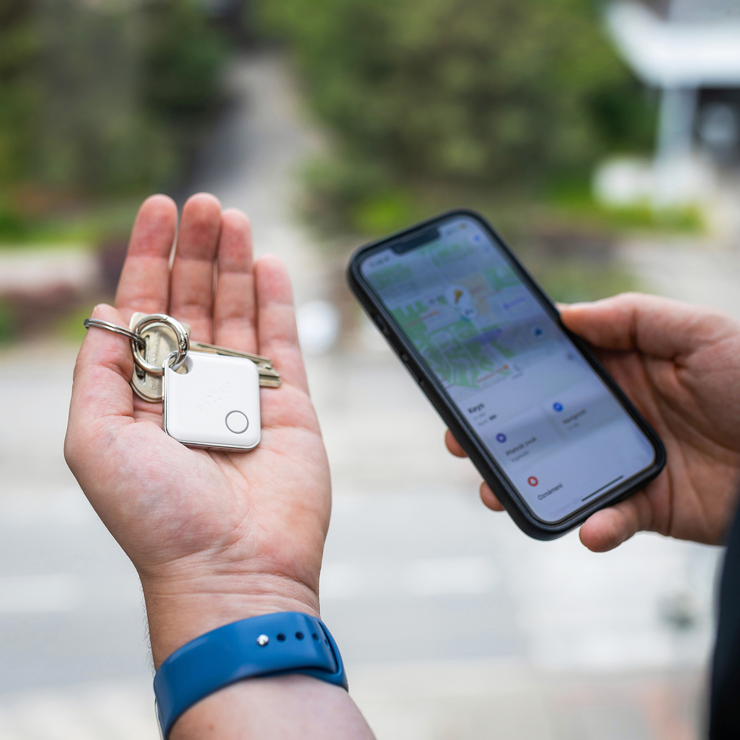 Eine Hand hält Schlüssel mit einem Tracker, die andere ein Smartphone mit Karten-App.