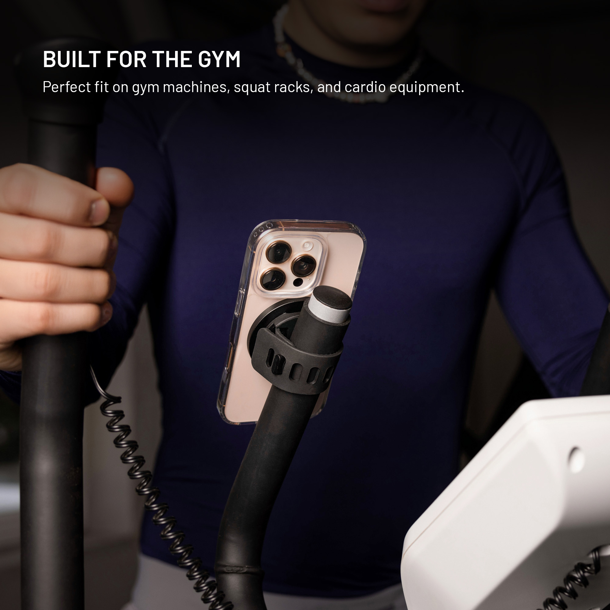 Ein Smartphone ist sicher an einer Stange eines Fitnessgeräts montiert, im Hintergrund ist eine Person zu sehen.