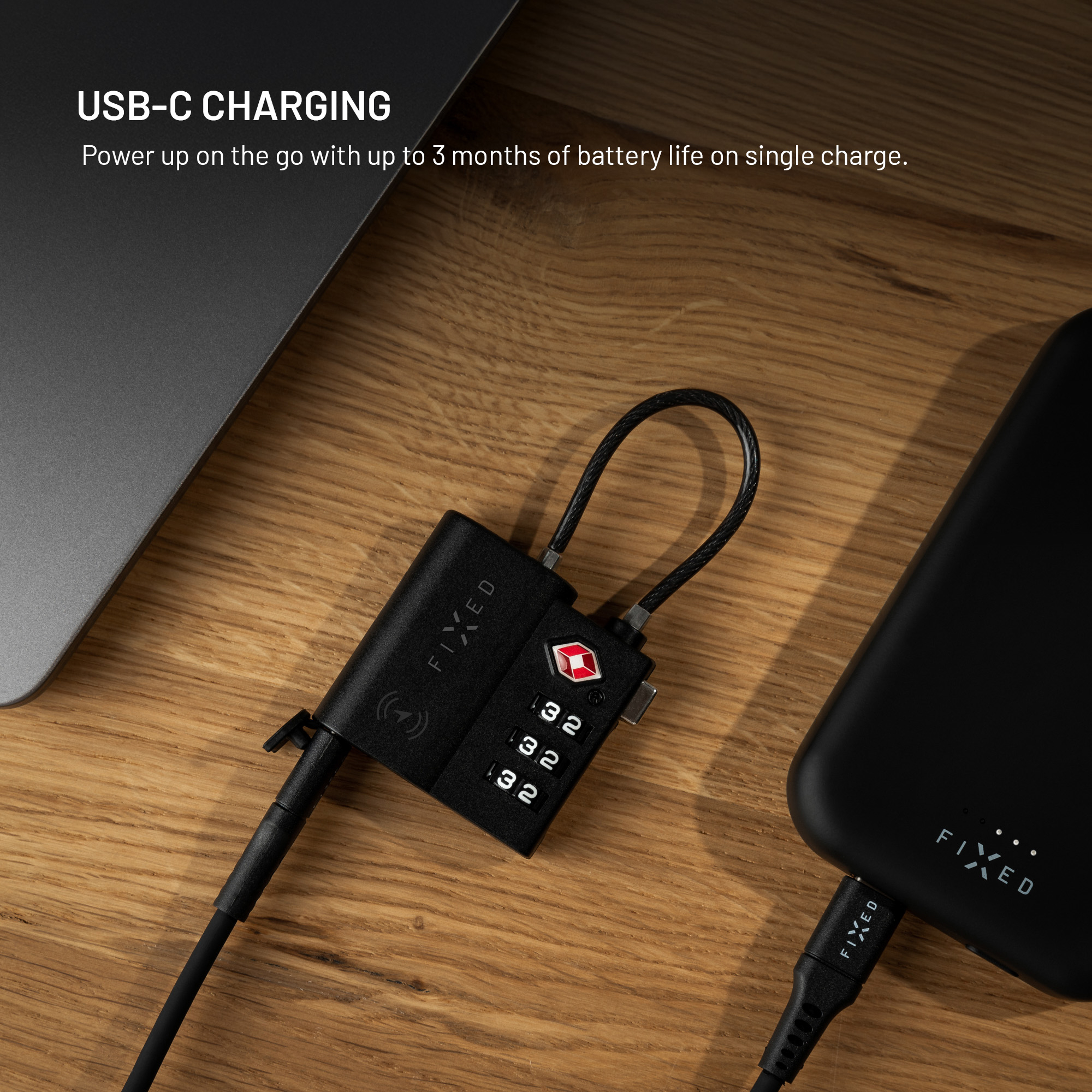 Ein schwarzes TSA-Zahlenschloss liegt mit einem USB-C-Kabel auf einer Holzoberfläche neben einem Laptop.