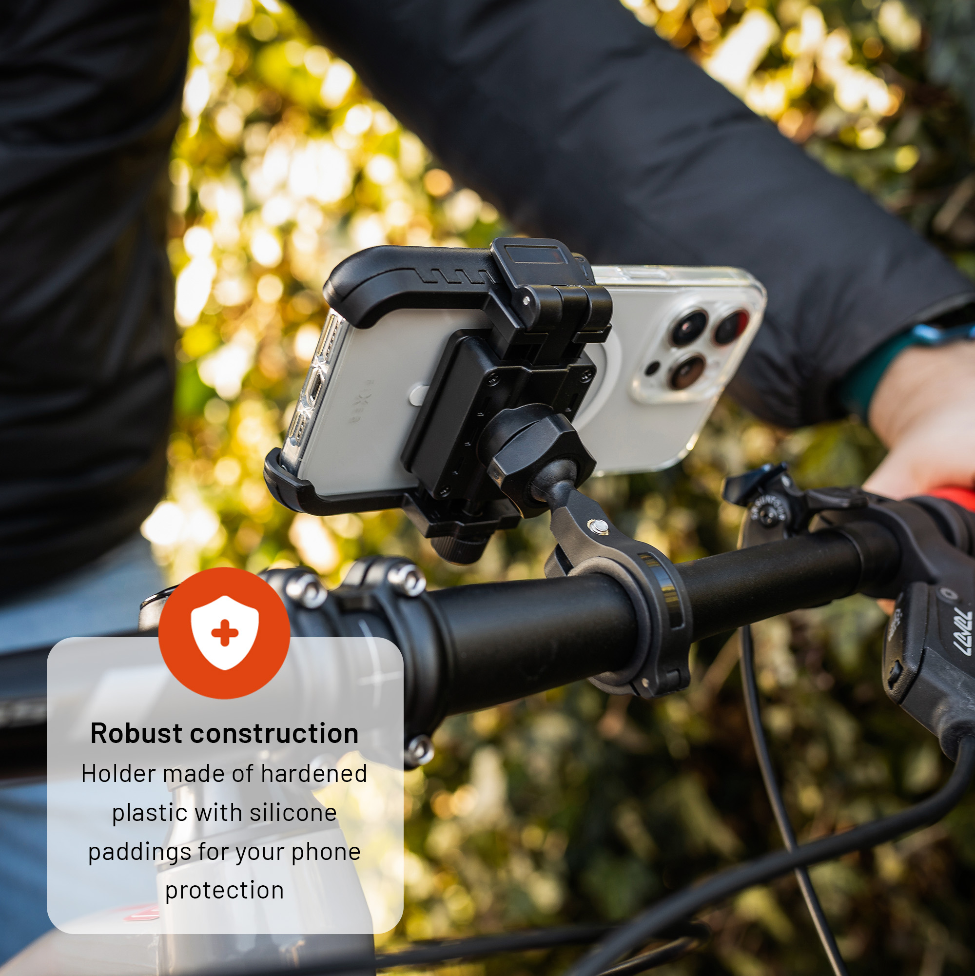Eine schwarze Smartphone-Halterung aus Kunststoff an einem Fahrradlenker hält draußen ein Handy mit Hülle.