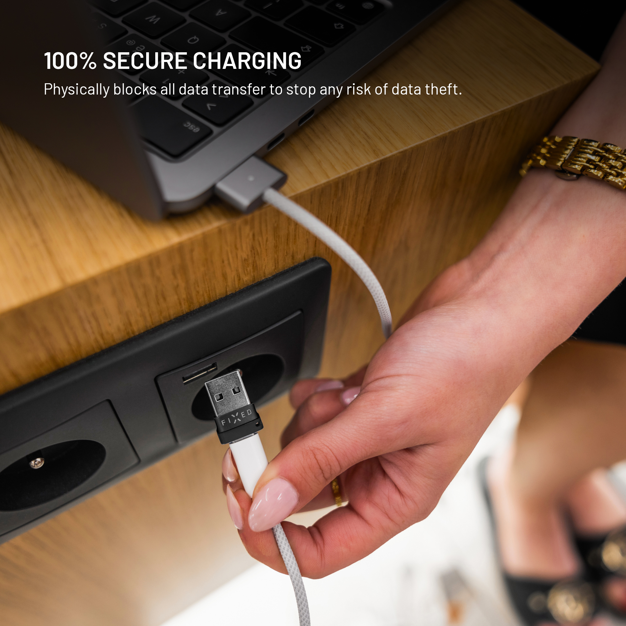Eine Person steckt ein weißes USB-Kabel in eine Steckdose neben einem Laptop.