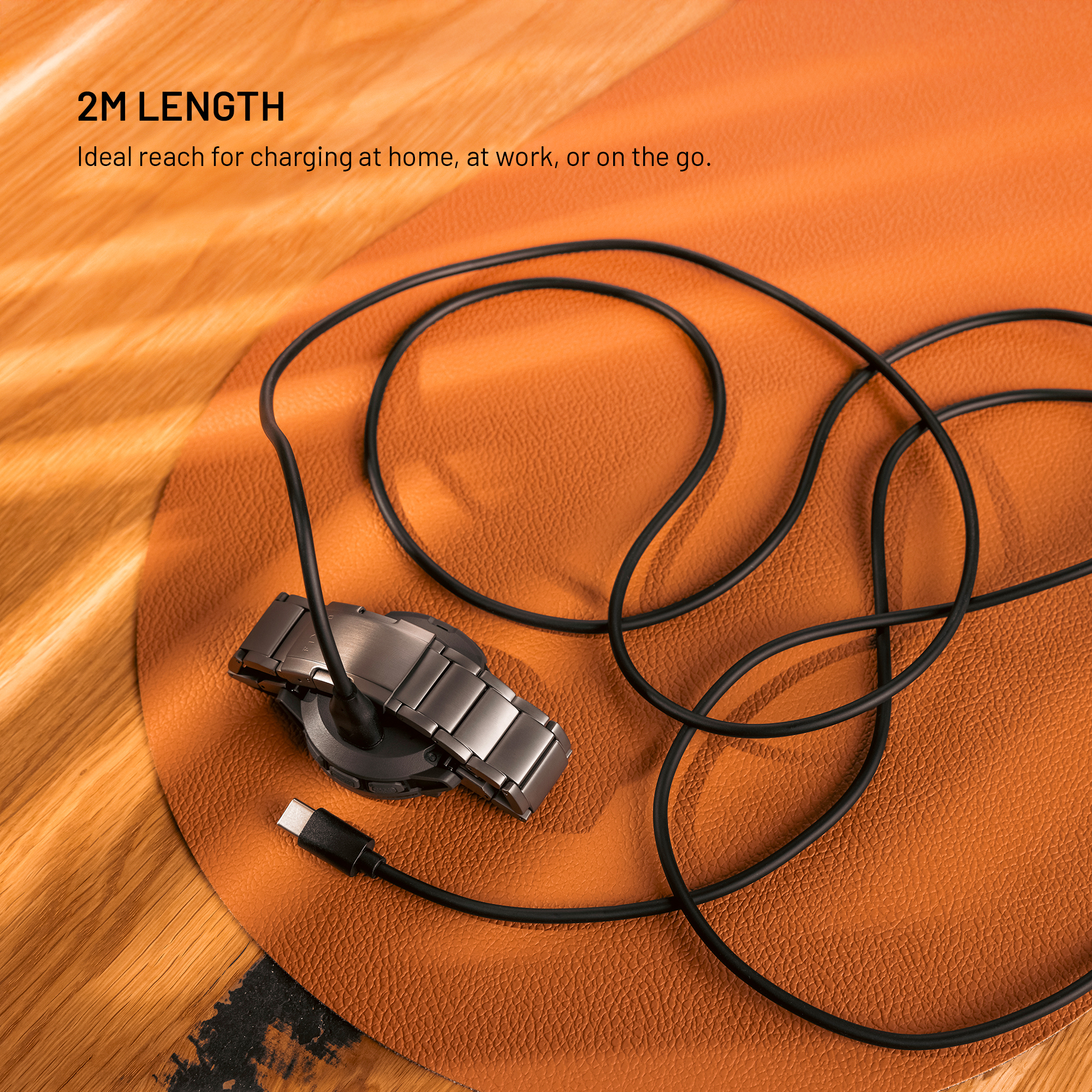Eine Smartwatch mit Metallarmband liegt mit einem langen schwarzen Ladekabel auf einer orangefarbenen Unterlage.