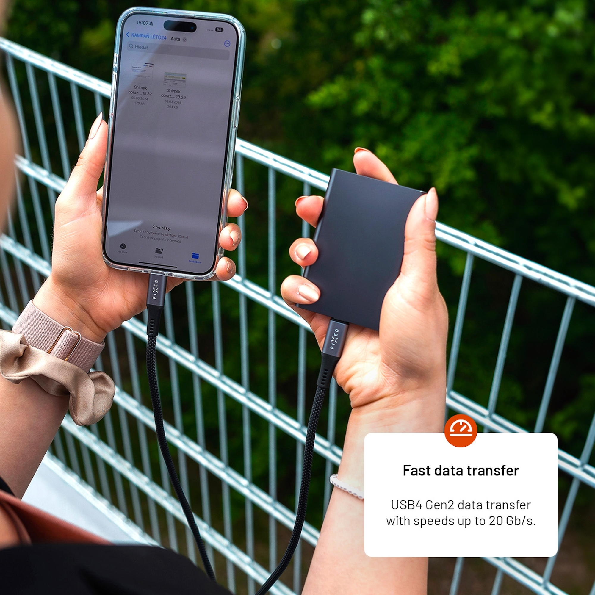 Eine Person hält ein Smartphone und eine externe SSD, die durch ein schwarzes Kabel verbunden sind.