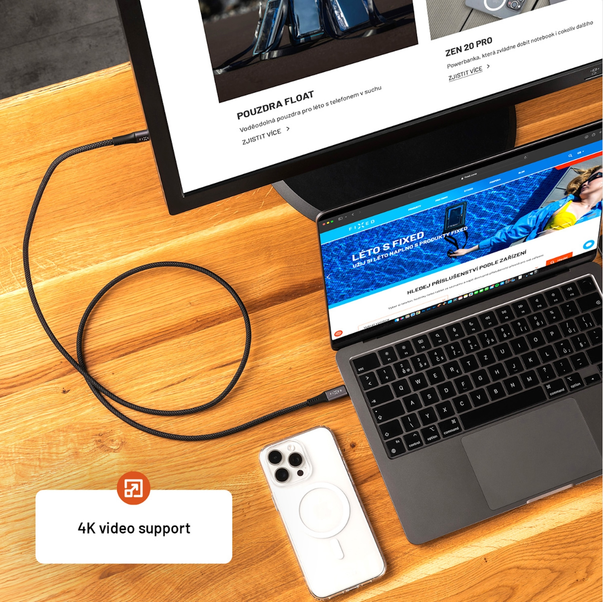 Ein Laptop, ein angeschlossener Monitor und ein Smartphone liegen mit einem schwarzen Kabel auf einem Holztisch.