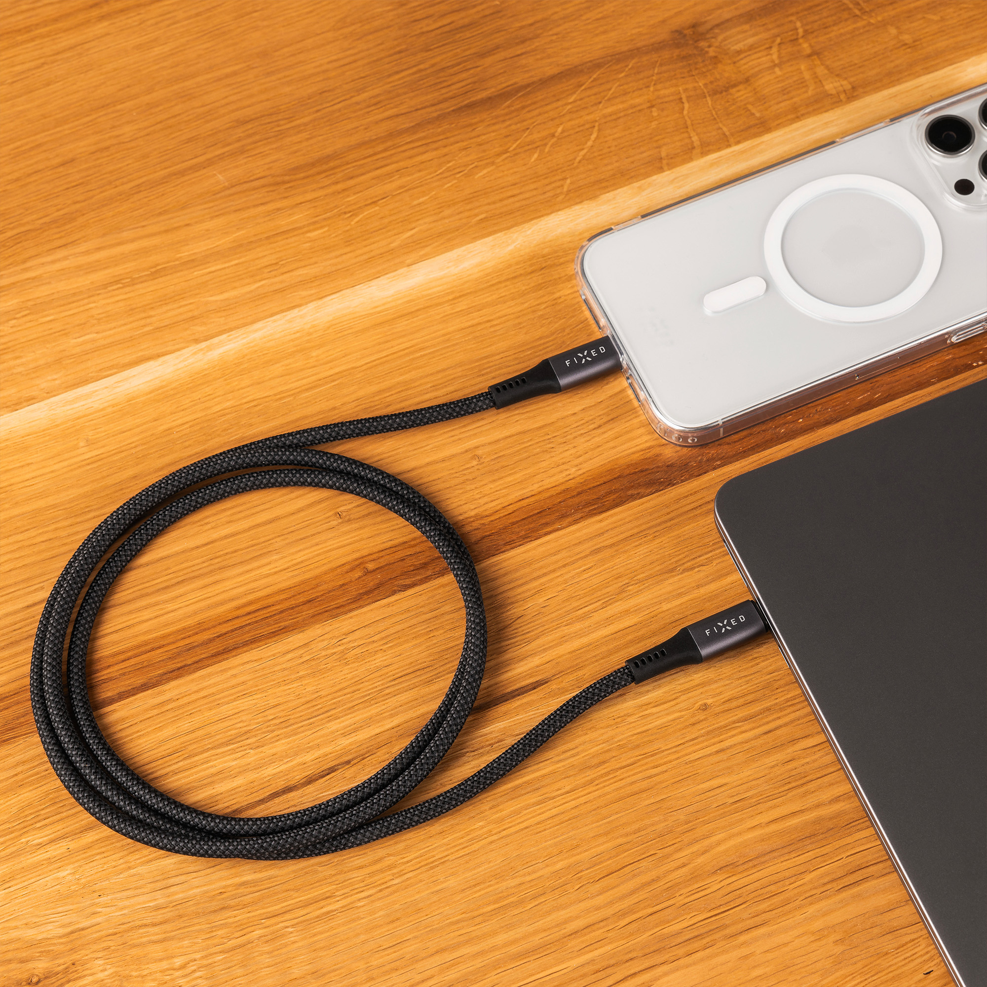 Ein gewebtes schwarzes Kabel verbindet ein Smartphone und einen Laptop auf Holz.