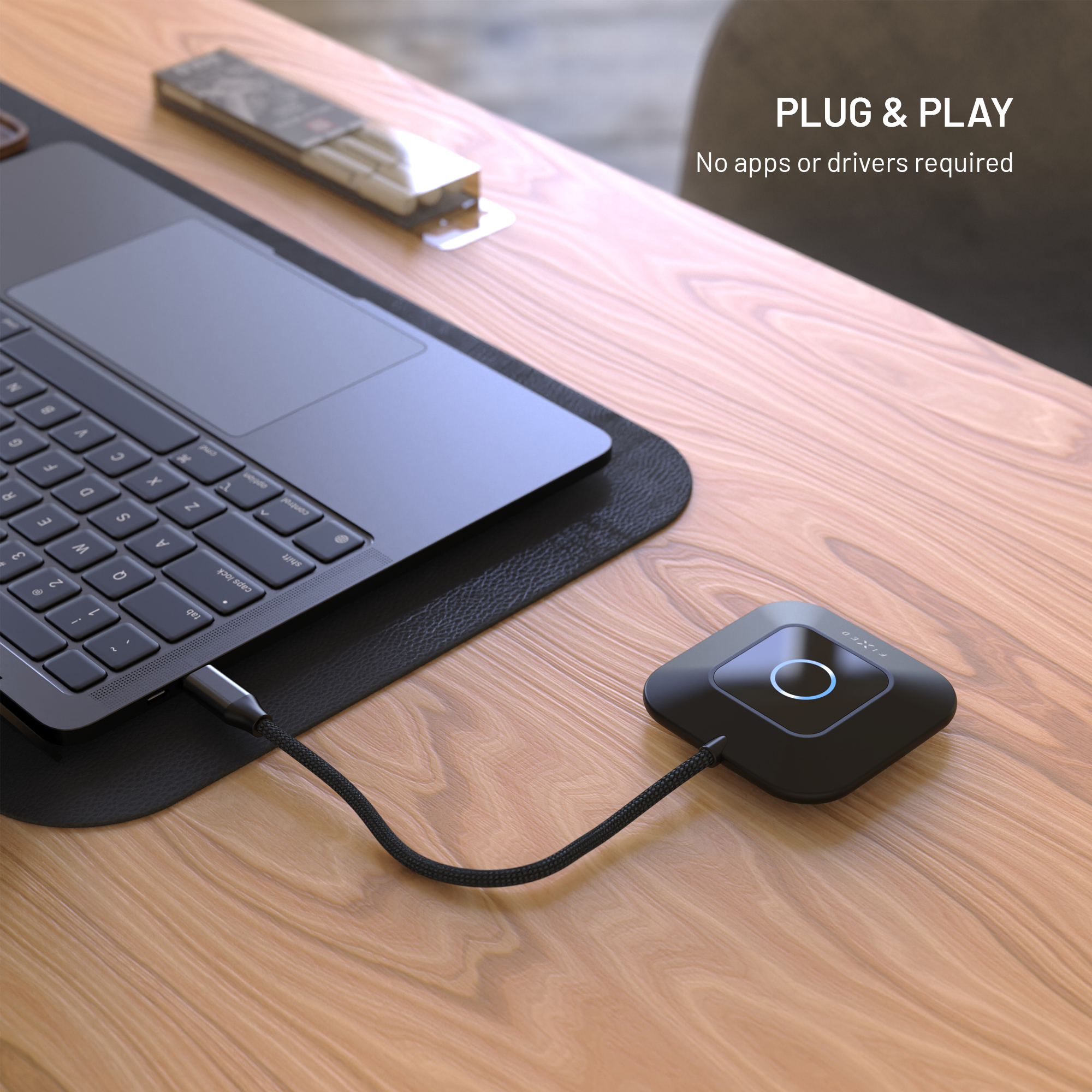 Ein schwarzes quadratisches Gerät, das über ein Kabel mit einem Laptop auf einem Holztisch verbunden ist.