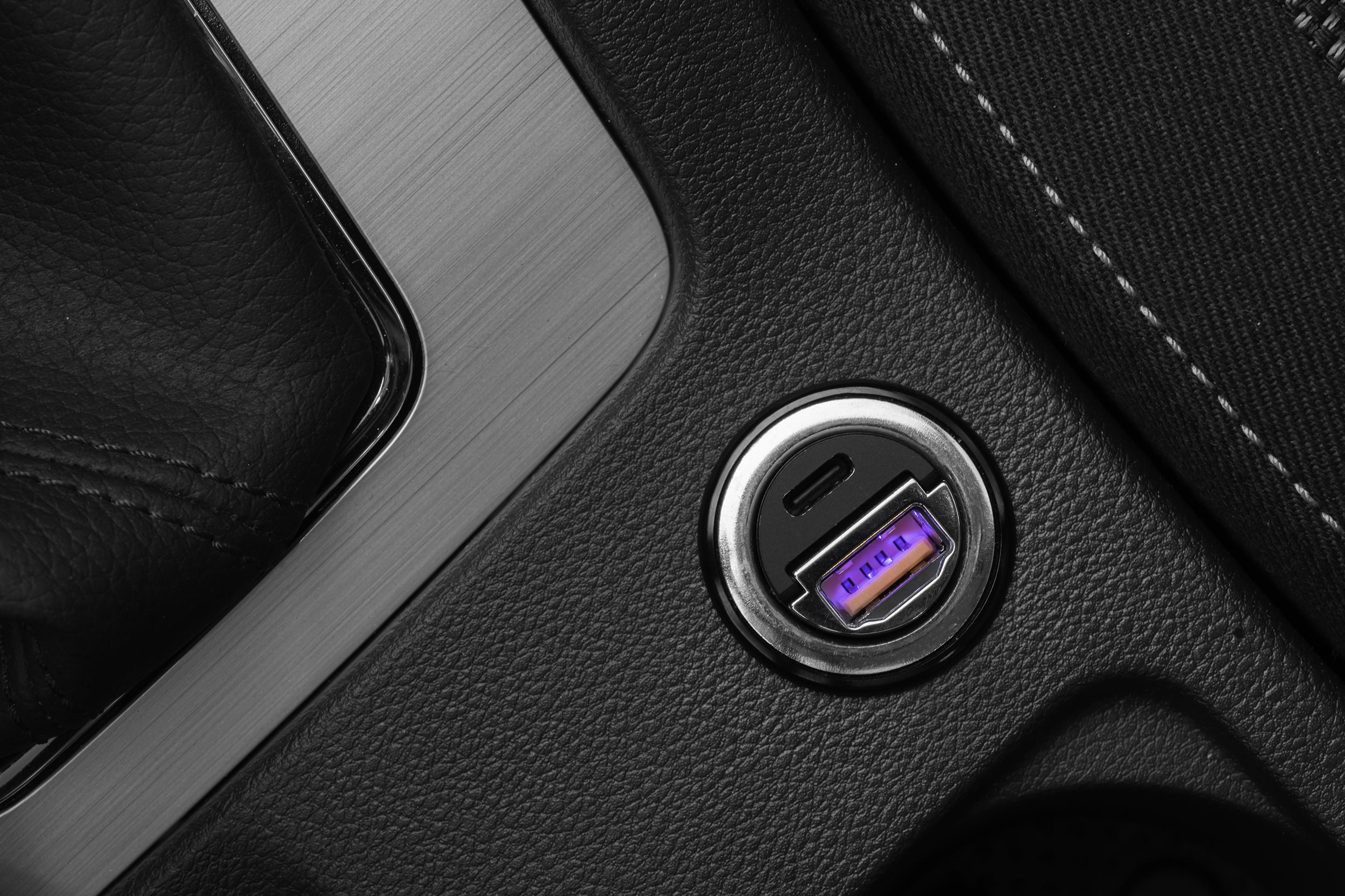 Ein Auto-USB-Anschluss mit violetter Beleuchtung in einer schwarzen Konsole neben Metall- und Lederdetails.