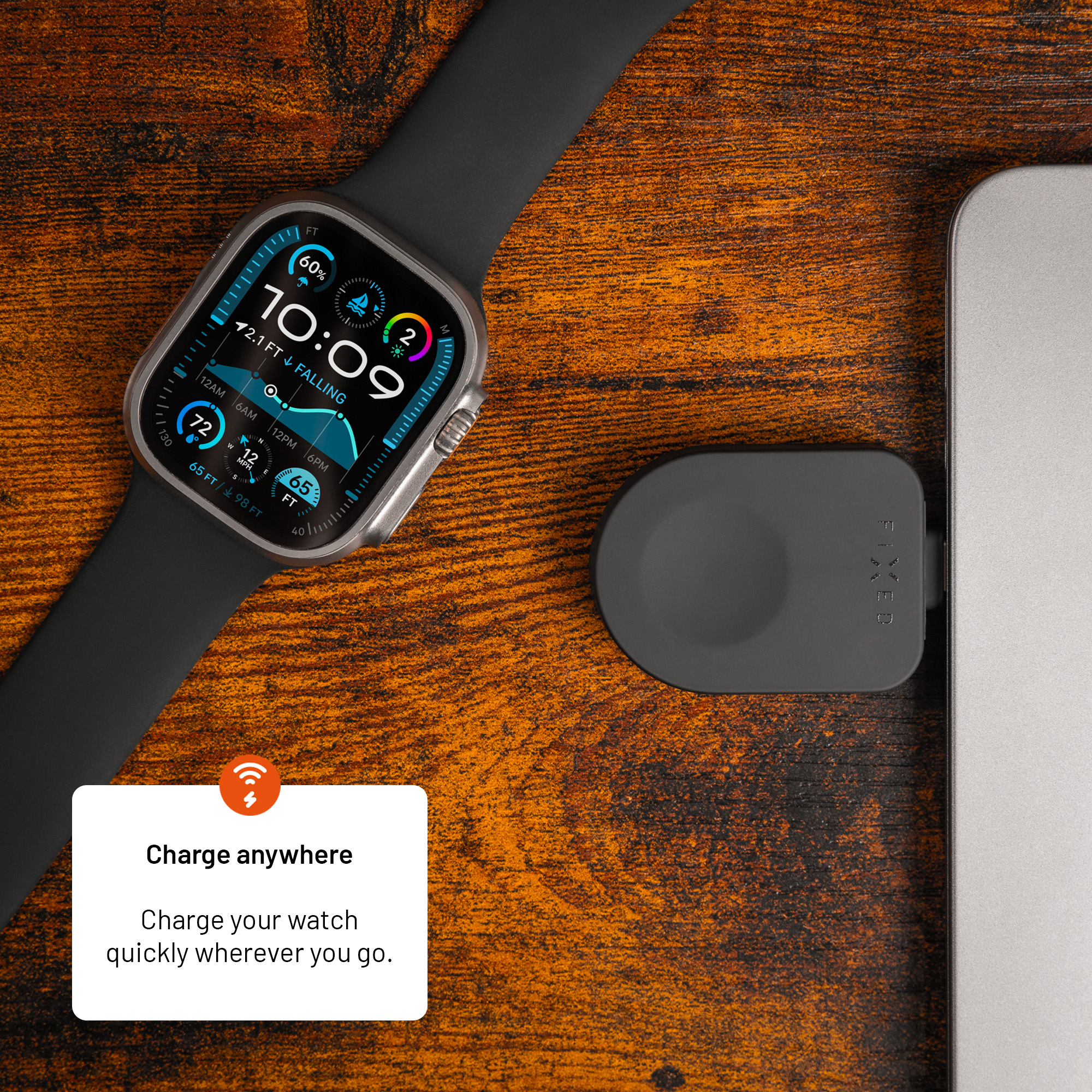 Eine Smartwatch liegt auf Holz neben einem Laptop, verbunden mit einem kleinen schwarzen Ladegerät.