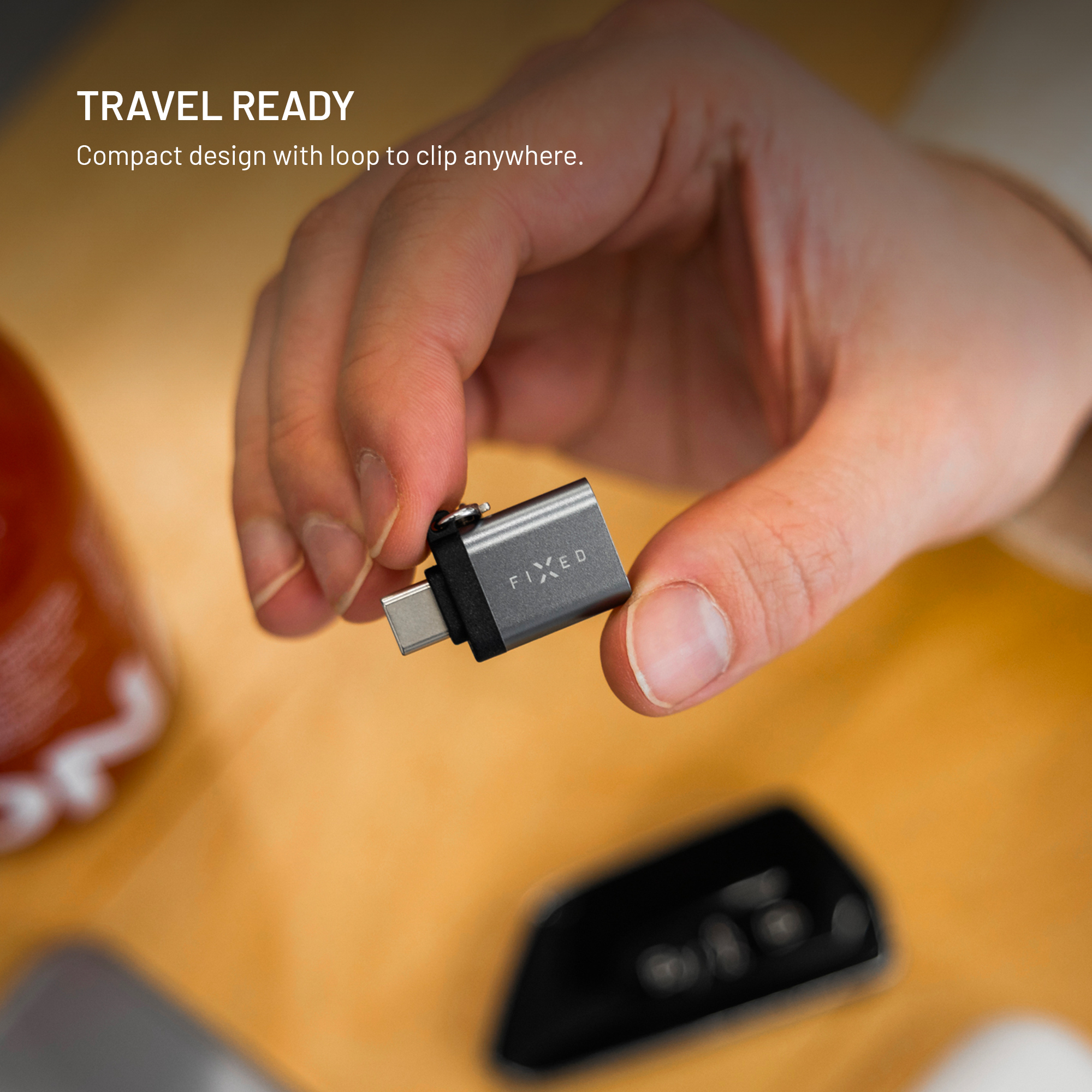 Eine Hand hält einen grauen USB-C-Adapter mit Clip vor einem holzfarbenen Hintergrund.