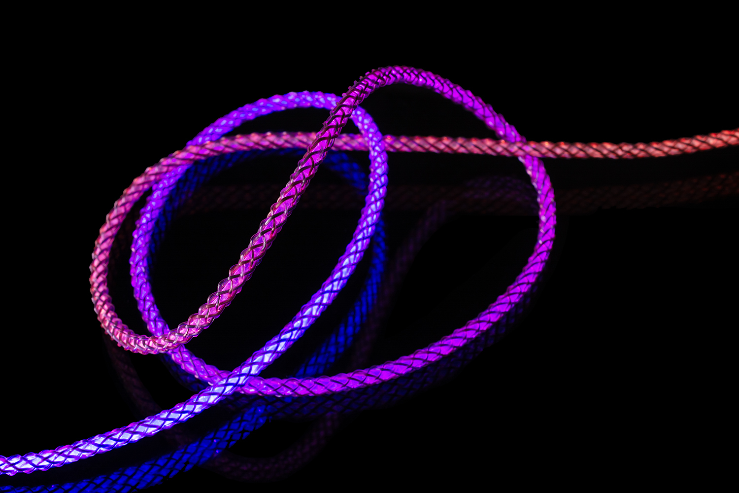 Ein glänzendes, geflochtenes Kabel leuchtet in lebendigen Violett- und Orangetönen auf einem schwarzen Hintergrund.
