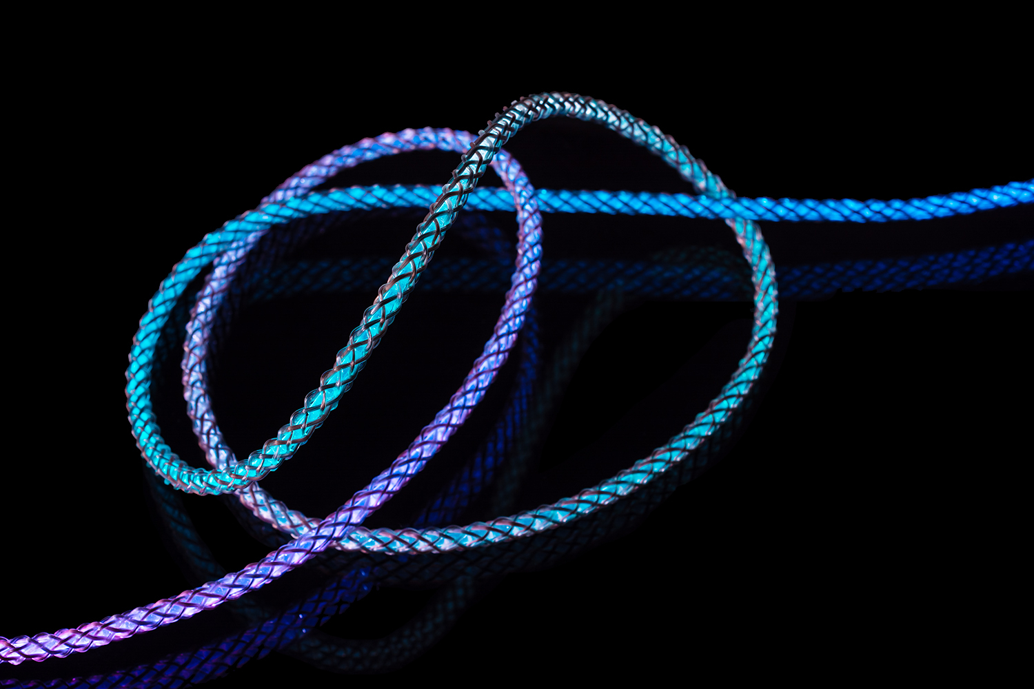 Ein blau und violett leuchtendes, geflochtenes Kabel liegt auf einer schwarzen, reflektierenden Oberfläche.
