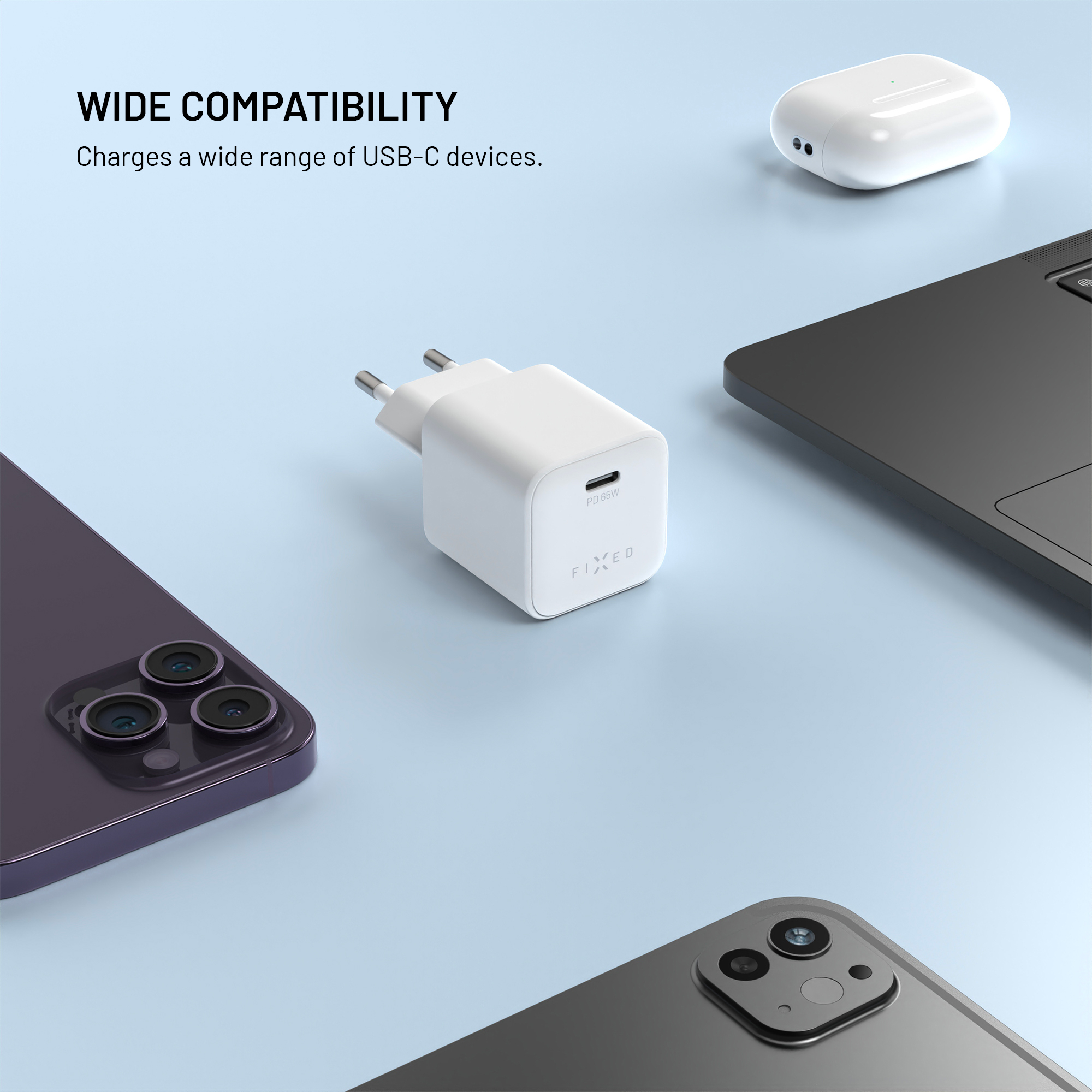 Ein weißes USB-C-Ladegerät liegt auf blauem Hintergrund, umgeben von Geräten wie Telefon und Laptop.