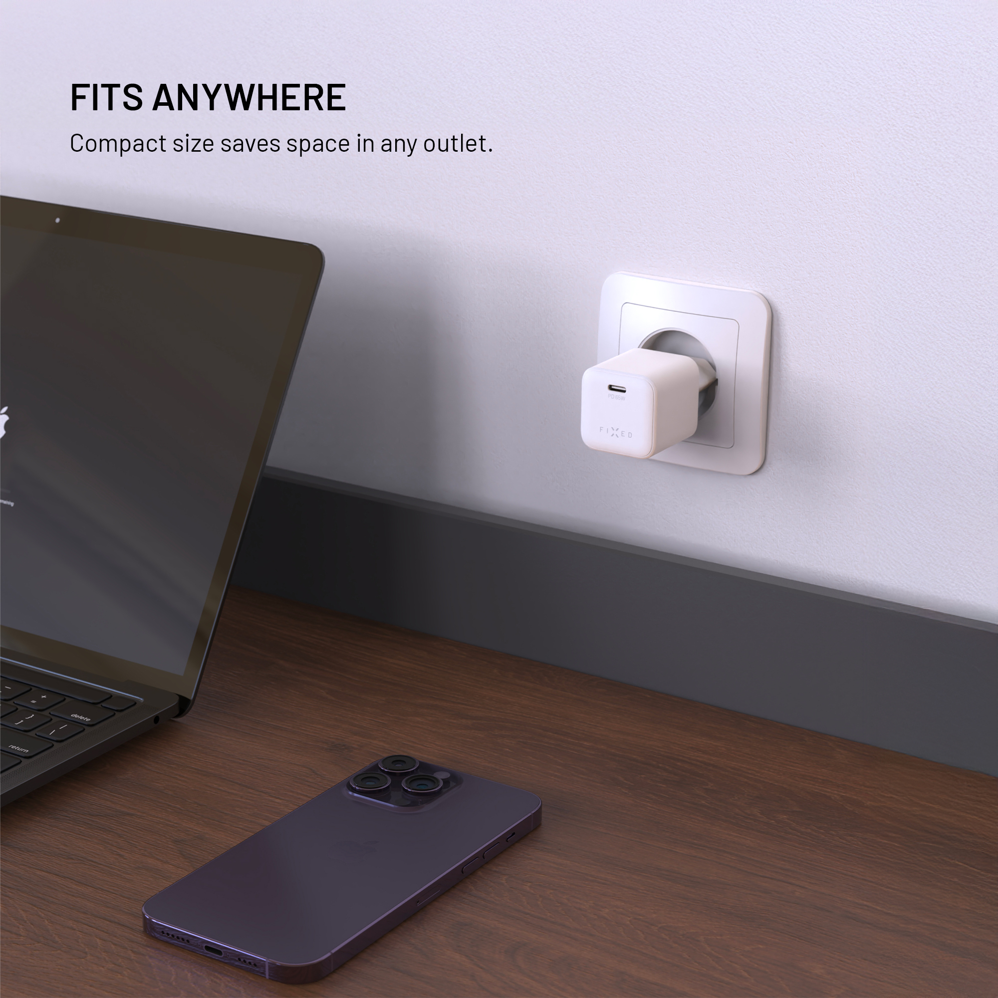 Kompaktes weißes USB-C-Ladegerät in Steckdose an der Wand, mit Laptop und Smartphone auf dem Tisch.