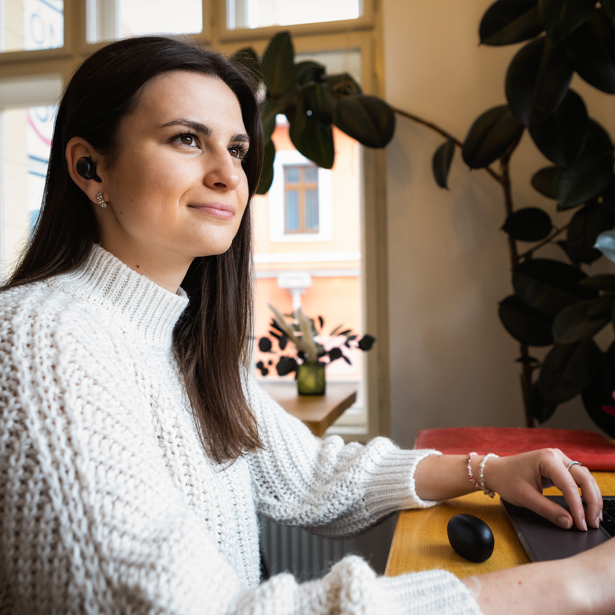 Eine junge Frau mit weißem Pullover arbeitet an einem Laptop und lächelt.