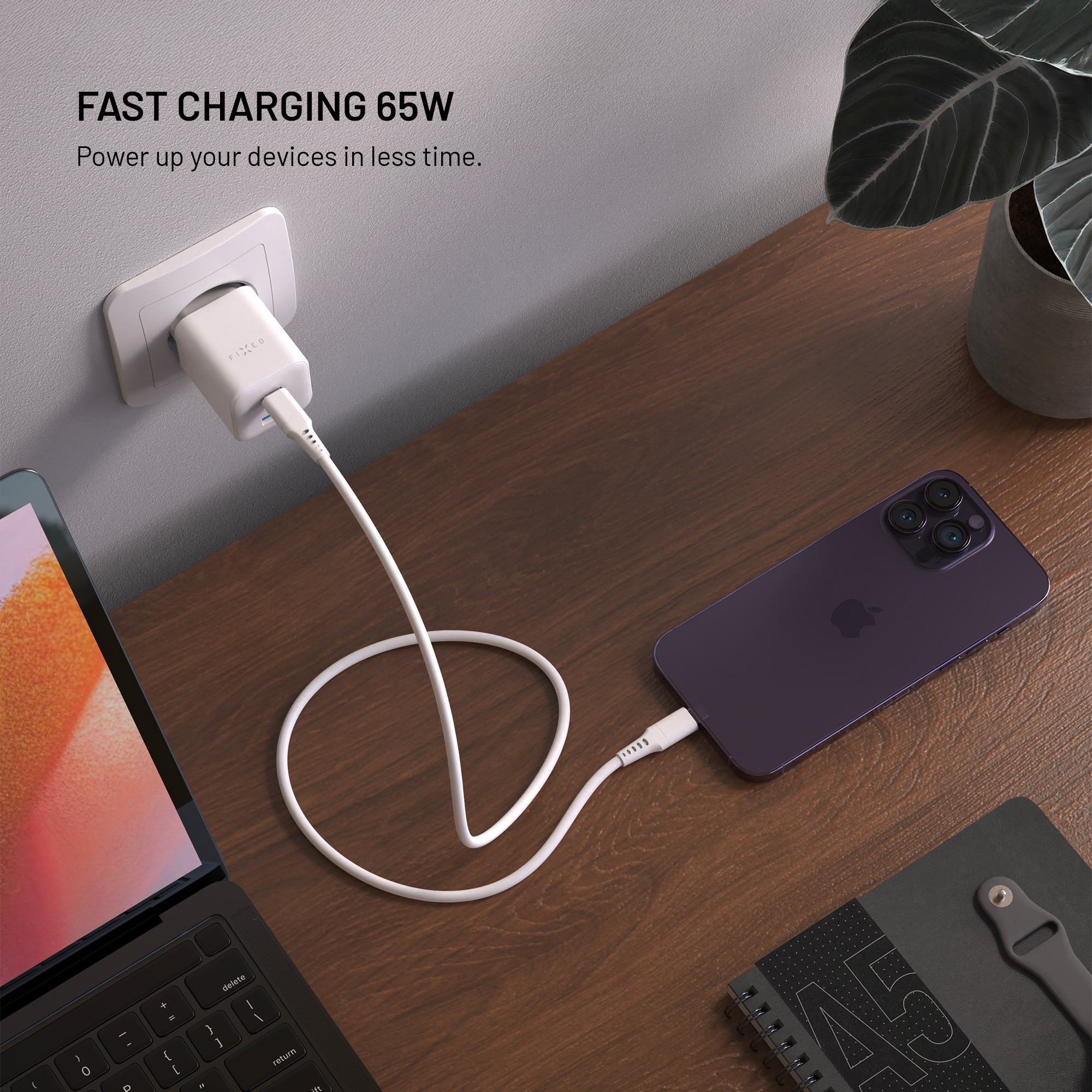 Ein weißes 65W-Ladegerät in der Wand, ein Kabel verbindet es mit einem dunkelvioletten Smartphone auf einem Holztisch.