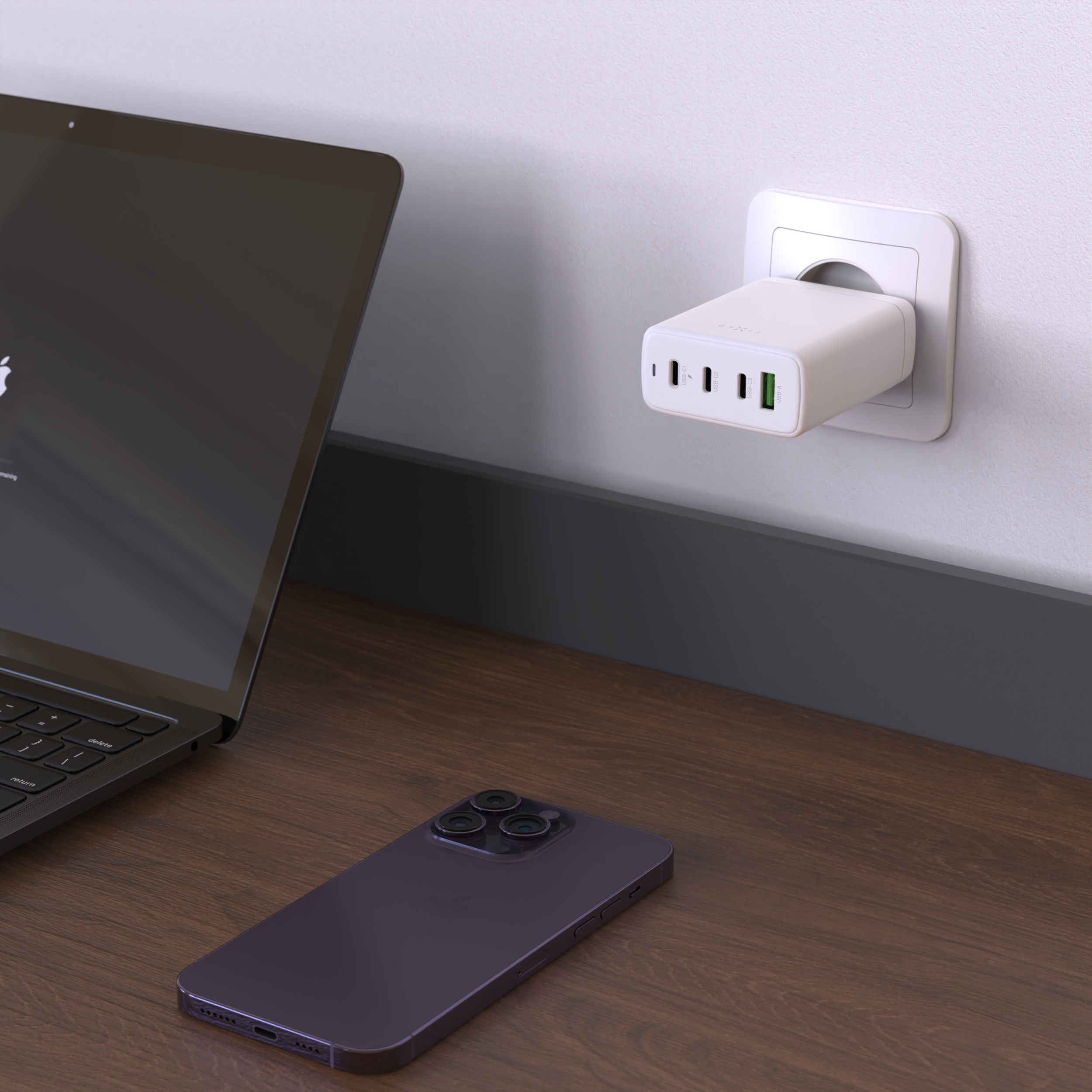 Ein weißes USB-Ladegerät in der Wandsteckdose über einem Schreibtisch mit Laptop und Smartphone.