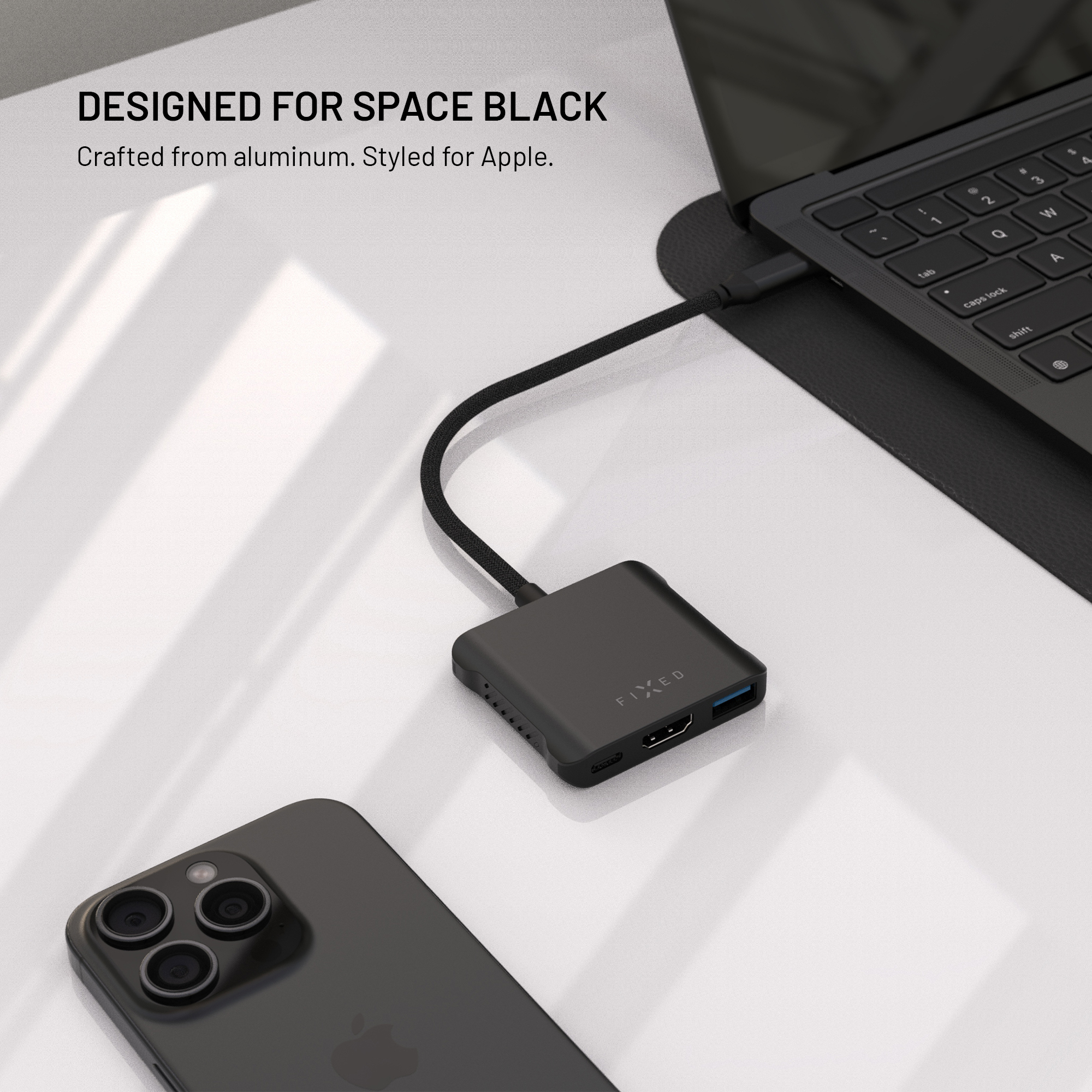 Ein schwarzer USB-C-Hub auf einem Schreibtisch neben einem Smartphone und einem Laptop.