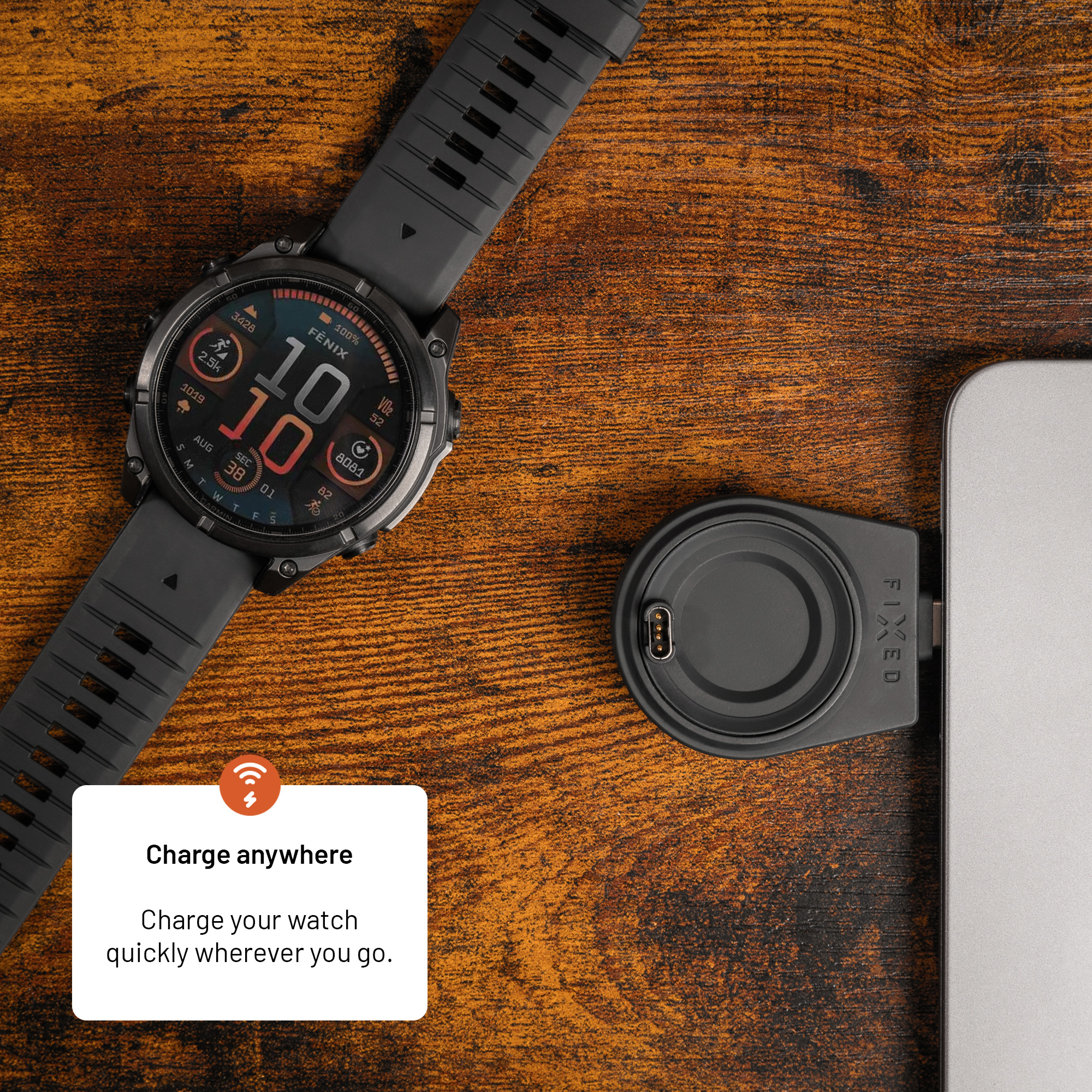 Eine schwarze Smartwatch liegt auf einem Holztisch neben einem Laptop mit eingestecktem Magnetlader.