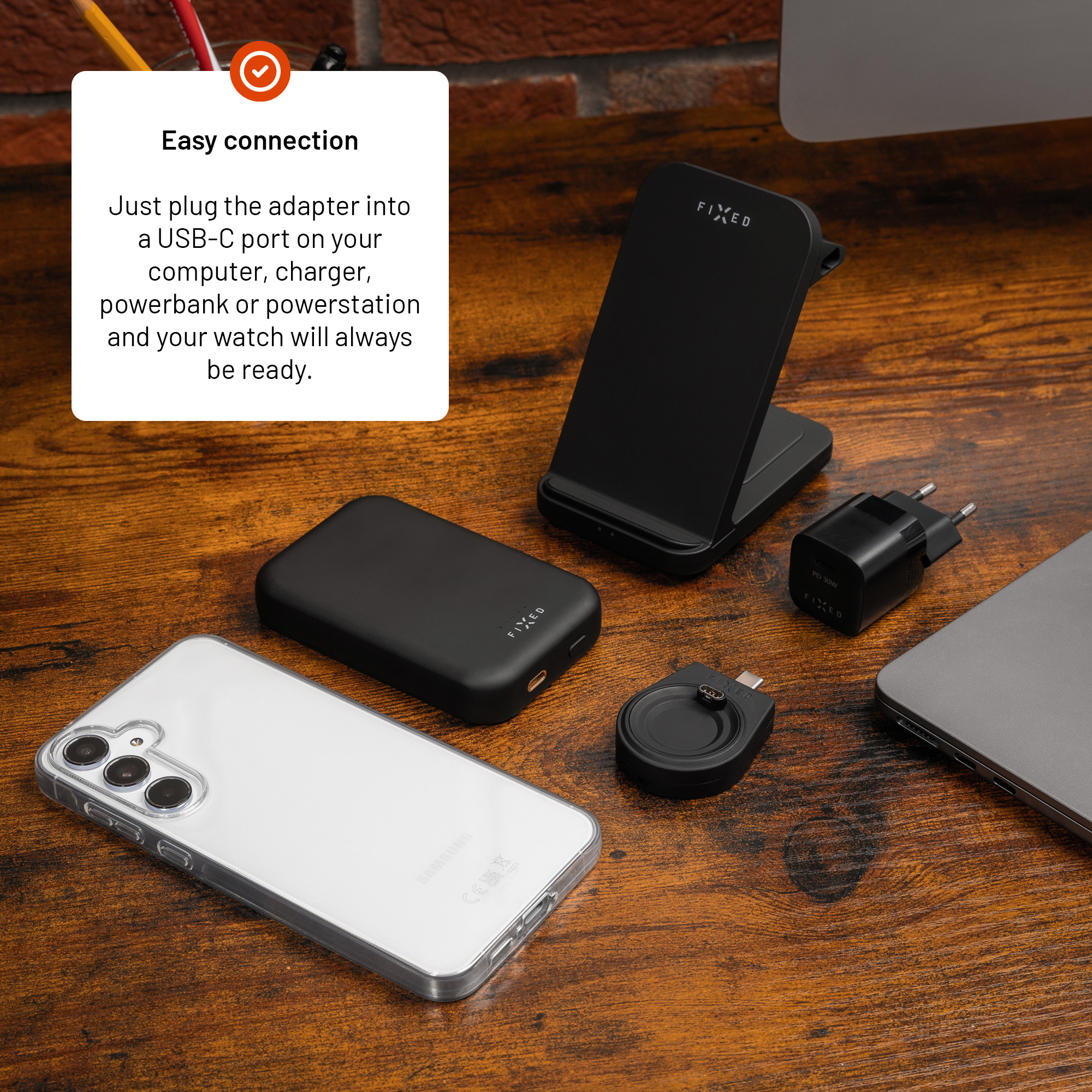 Schwarzes Zubehör wie Smartphone, Powerbank und Ladestation auf Holztisch mit Textfeld.