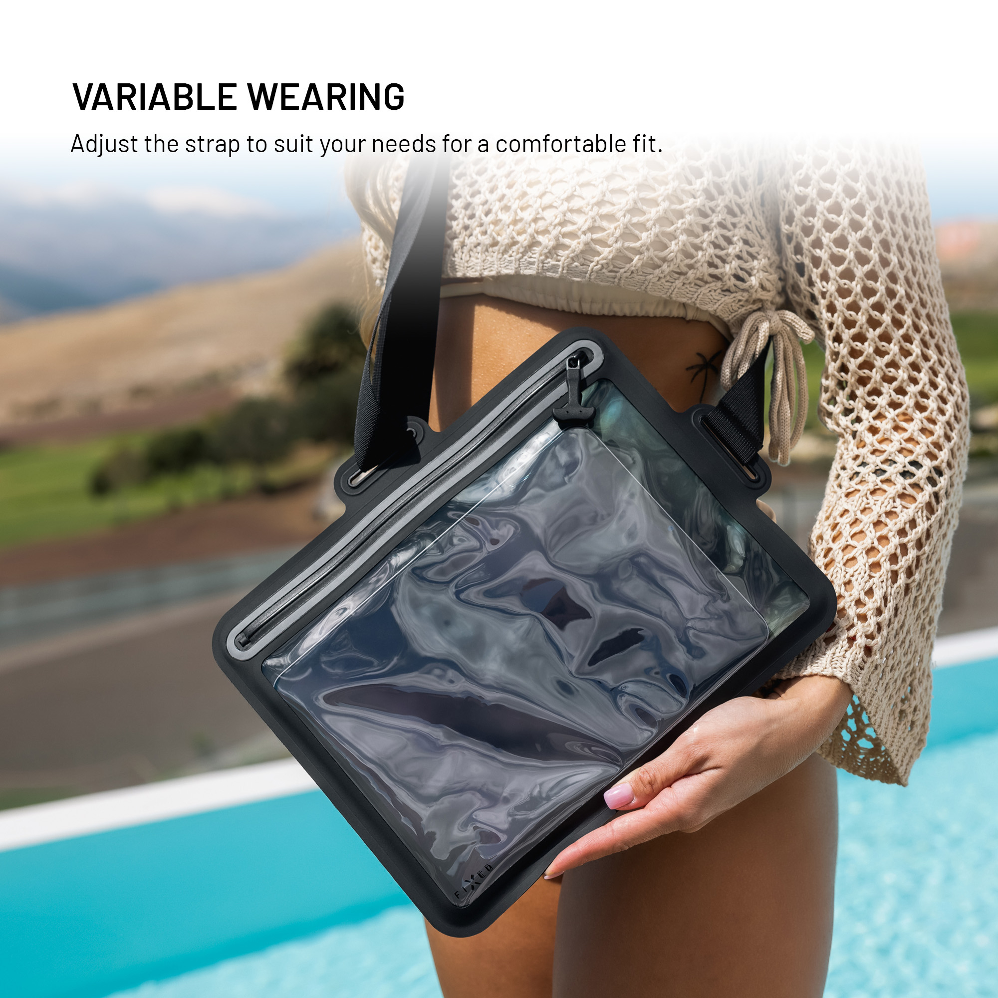 Eine Frau trägt eine schwarze, transparente Tasche mit Umhängegurt vor einer Pool- und Bergkulisse.