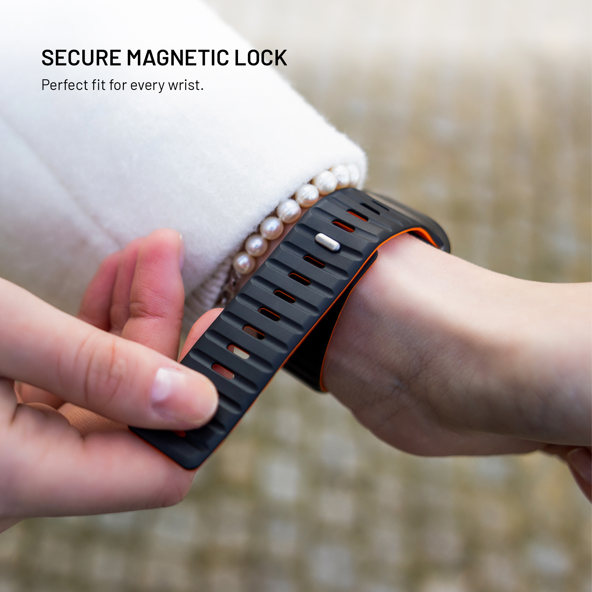 Una persona lleva una correa de reloj negra y naranja en la muñeca, con texto arriba que dice SECURE MAGNETIC LOCK.
