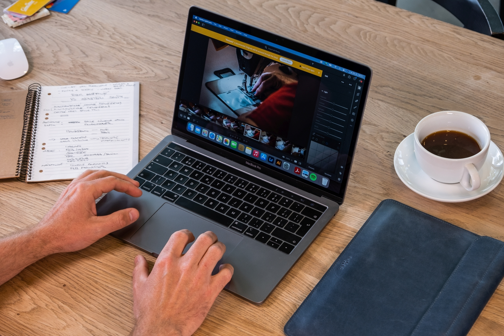 Ein Benutzer tippt auf einem MacBook Pro auf einem Holztisch, neben einem Notizbuch und einer Tasse Kaffee.