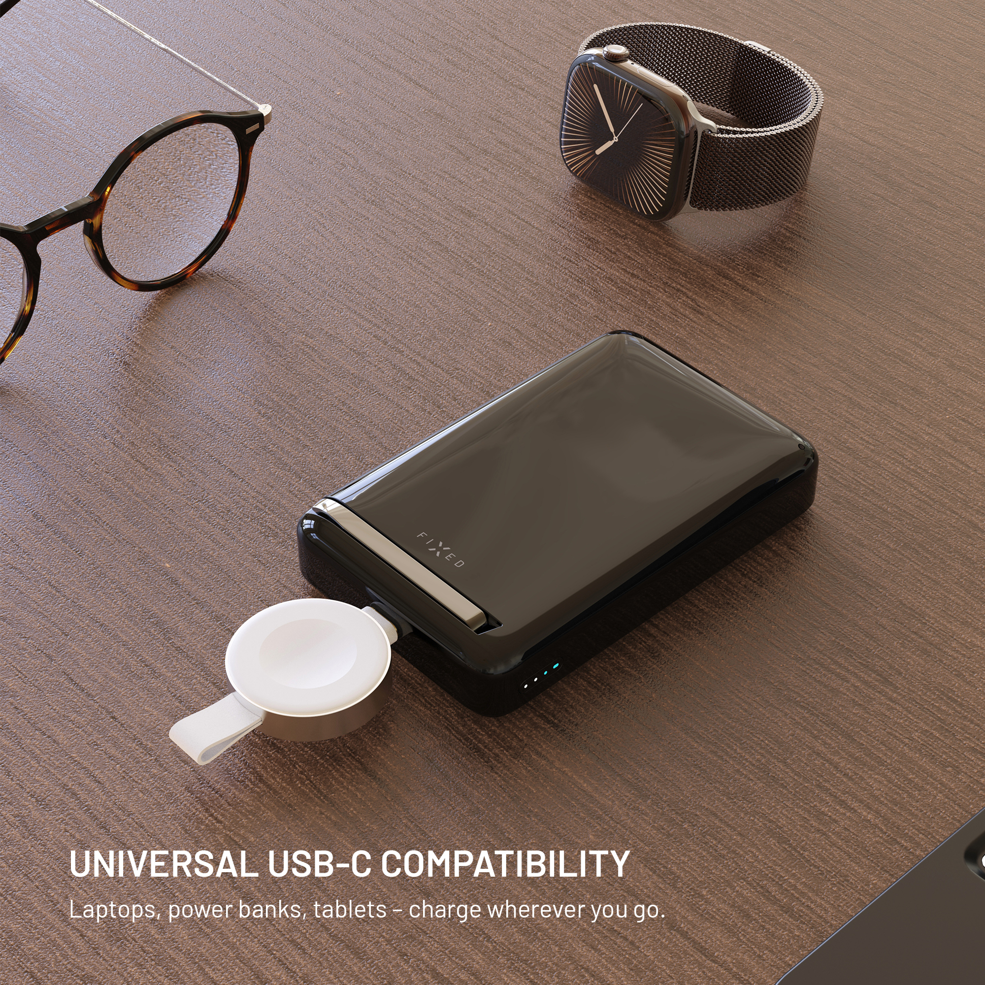 Eine schwarze Powerbank, Smartwatch und Brille auf einem Holzschreibtisch.