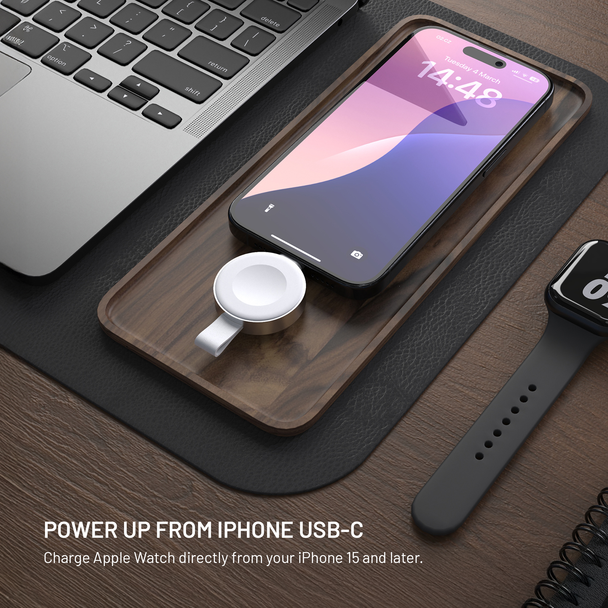 Ein Smartphone auf einem Holztablett mit Lade-Puck, neben Laptop und Uhr.