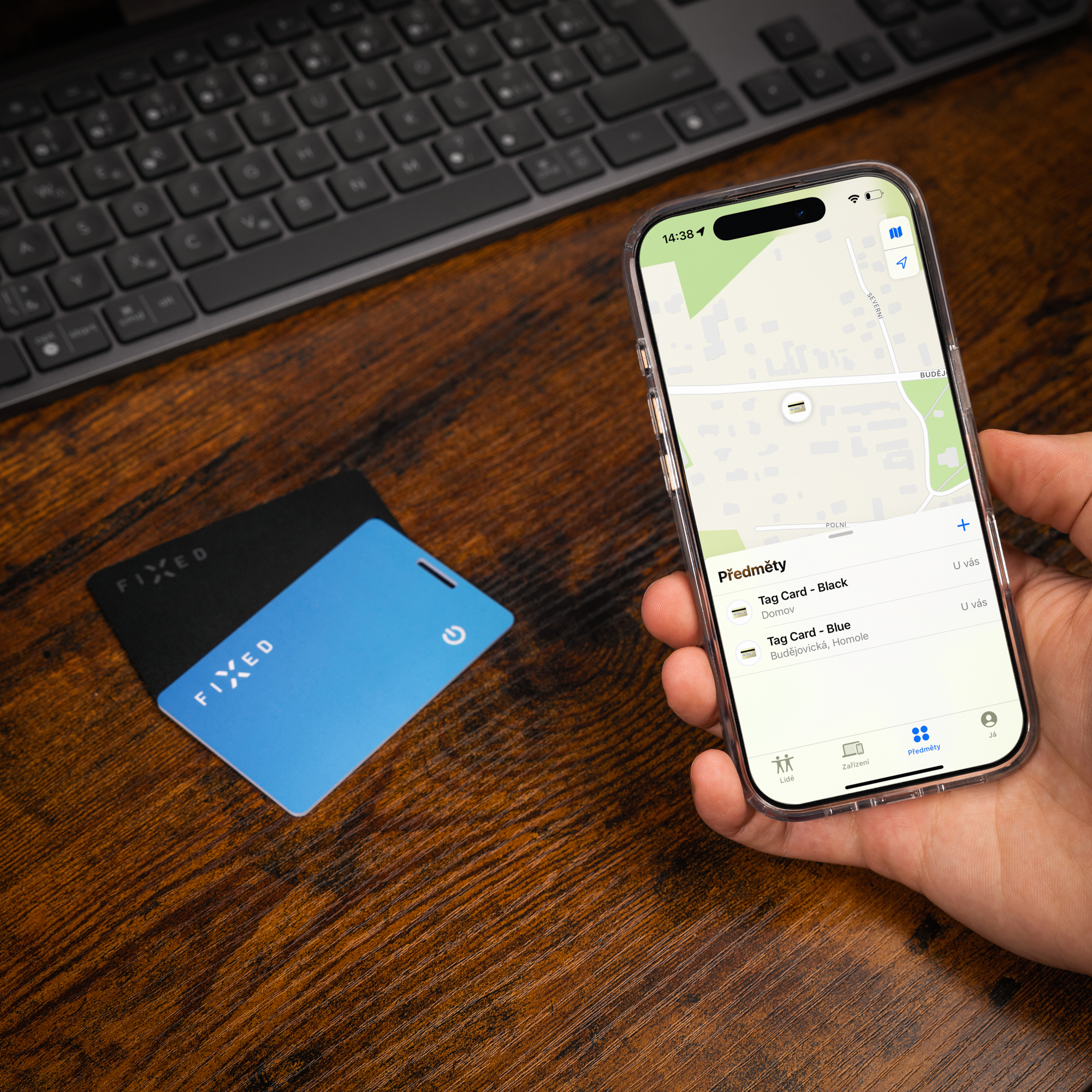 Smartphone mit Tracking-App in Hand, daneben zwei Fixed-Tag-Karten und eine Tastatur auf Holz.