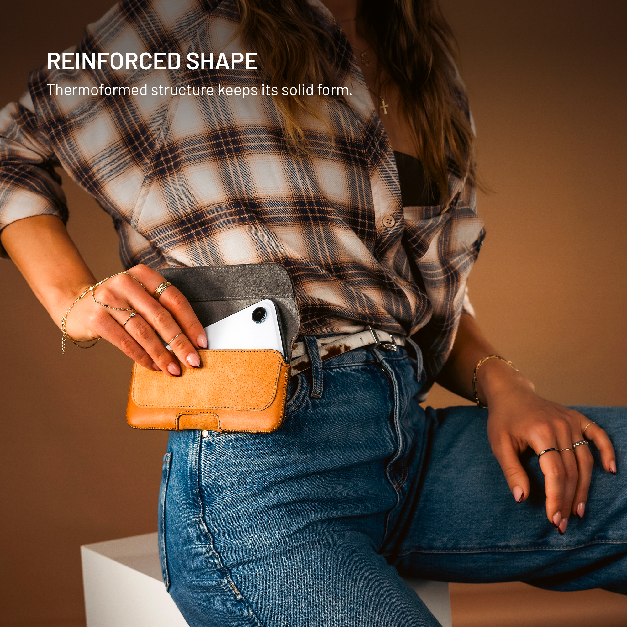 Eine Frau in Jeans und kariertem Hemd zieht ein weißes Handy aus einem braunen Lederholster.