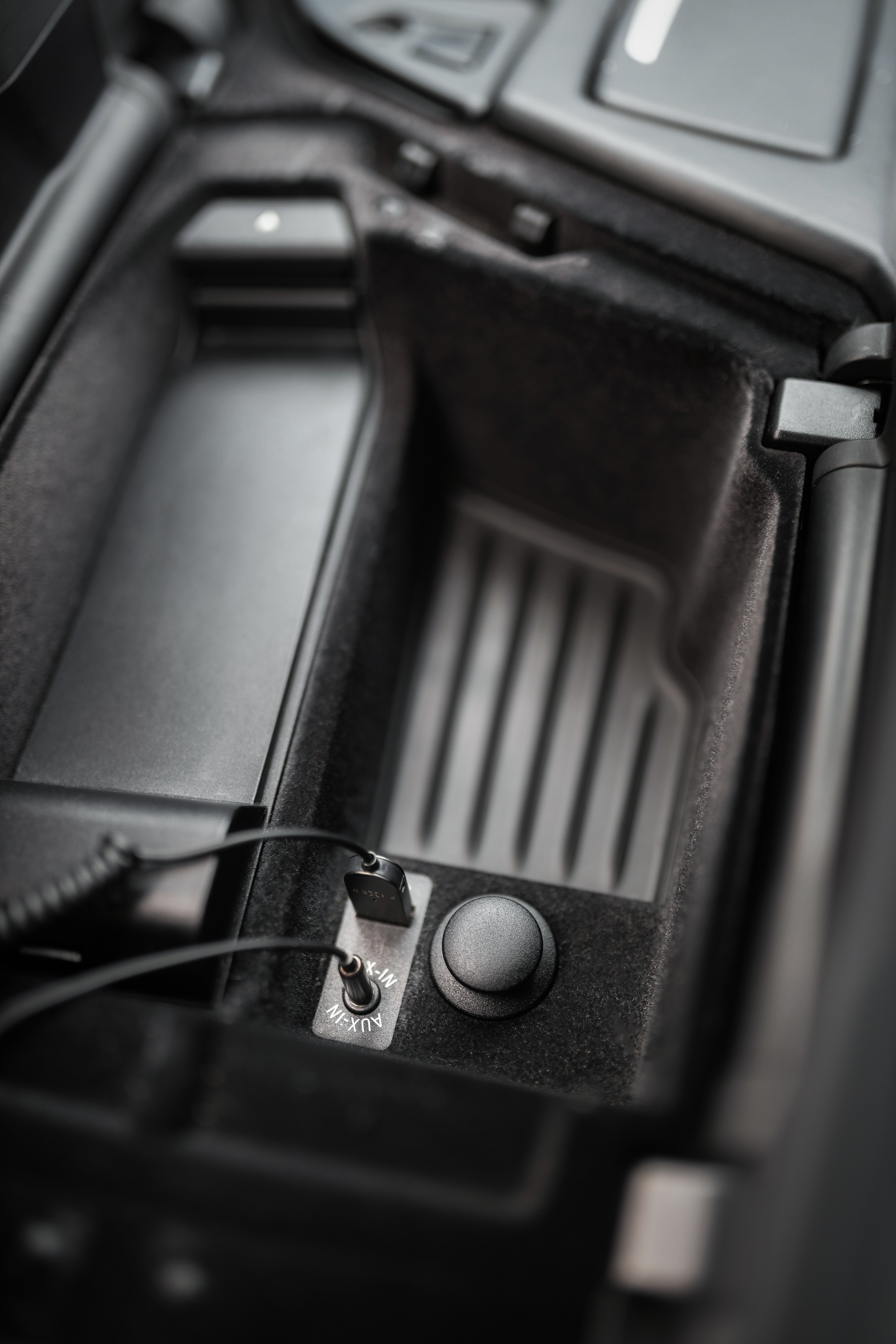 Innenansicht eines Auto-Mittelkonsolenfachs mit USB- und AUX-Anschlüssen sowie eingesteckten Kabeln.