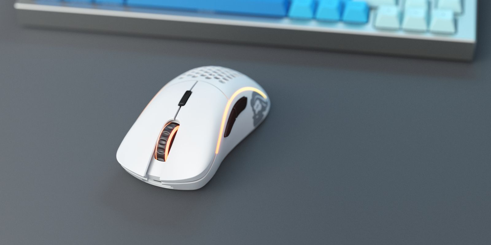 Eine weiße Computermaus mit orange leuchtenden Lichtern liegt auf einem grauen Schreibtisch, im Hintergrund eine Tastatur.
