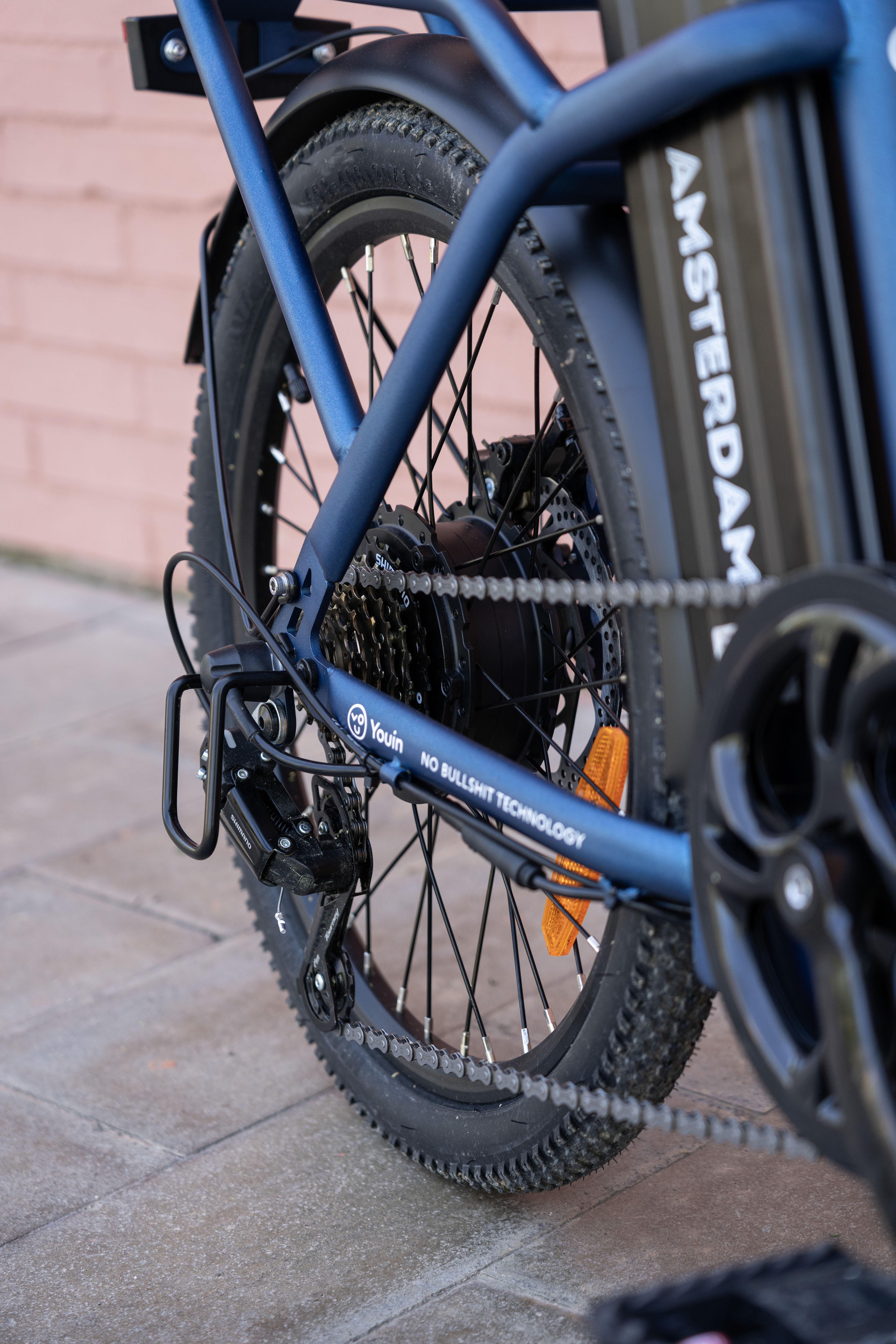 Primer plano de la rueda trasera de la bicicleta eléctrica azul con cadena, engranajes y batería.