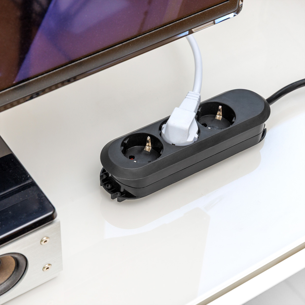 Eine schwarze Steckdosenleiste mit eingestecktem weißem Stecker liegt auf einer weißen Oberfläche.
